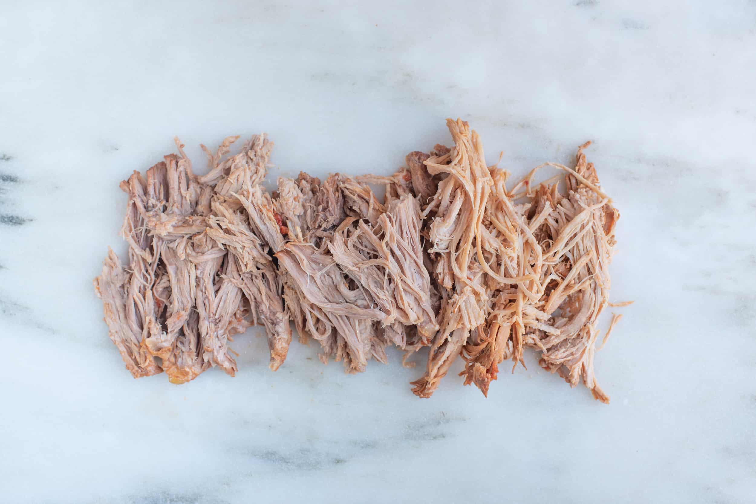 shreds of pulled pork spread out on a white background for babies starting solids