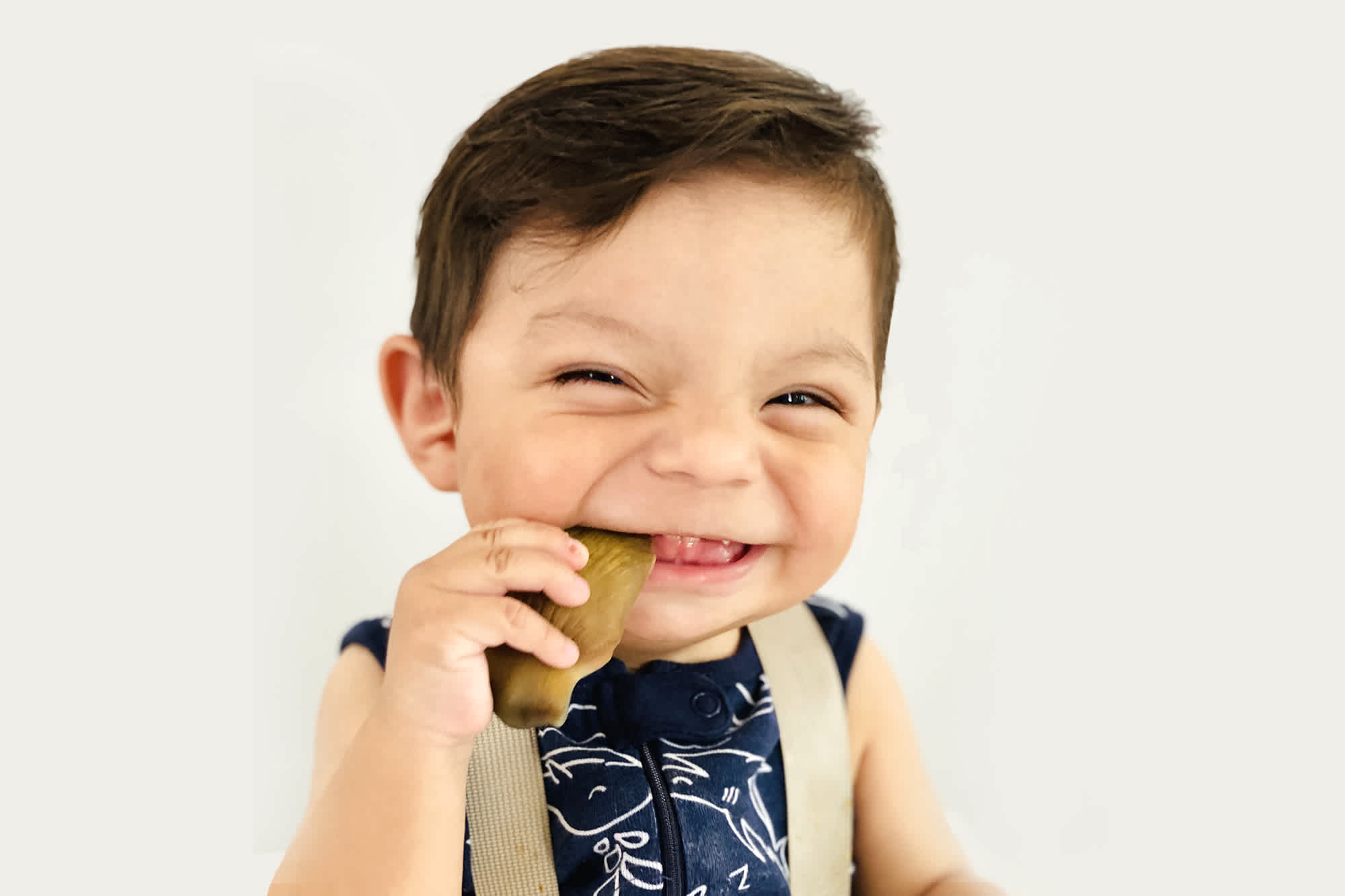 a smiling baby holding artichoke in her mouth