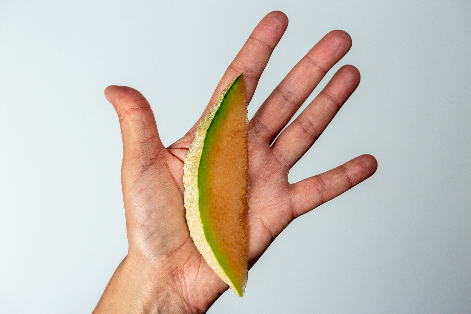 a hand holding a wedge of cantaloupe with the rind on