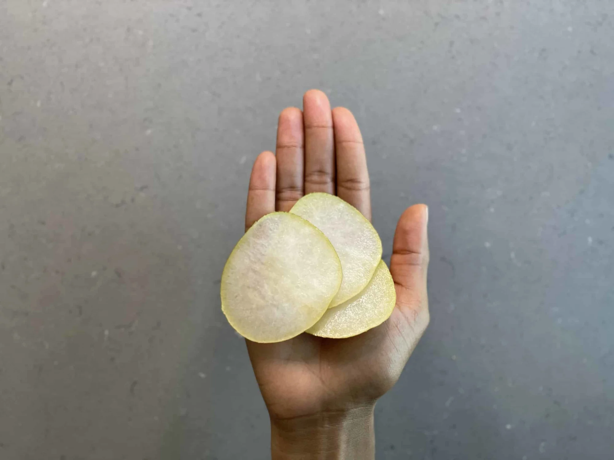 a hand holding paper-thin rounds of Asian pear for babies 9 months+