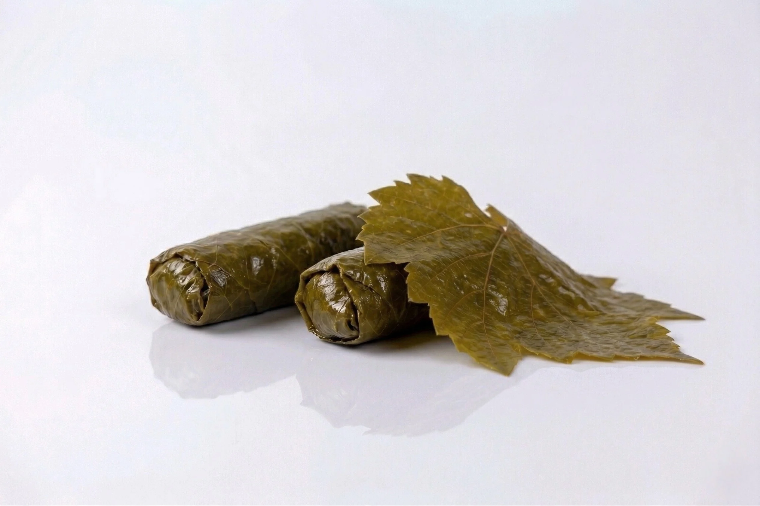 a photograph of two stuffed grape leaves with a whole brined leaf resting on them