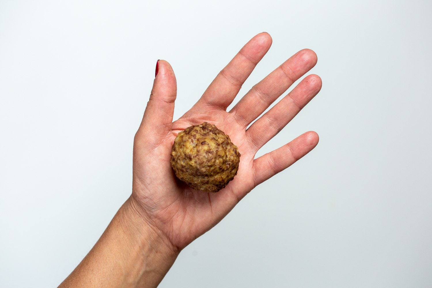 A hand holding a large soft meatball for babies 6 mos+