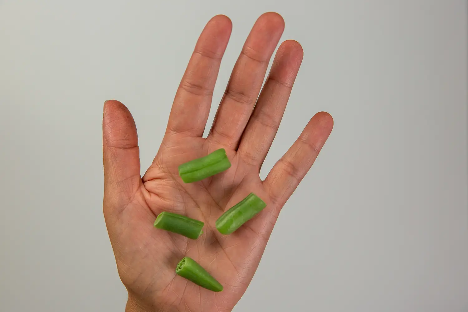 a hand holding bite-sized pieces of cooked green beans for children 12 months+