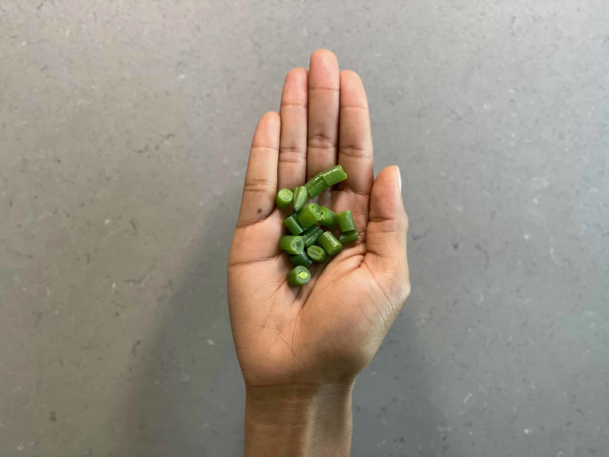 a hand holding bite-sized pieces of cooked green beans for children 12 months+