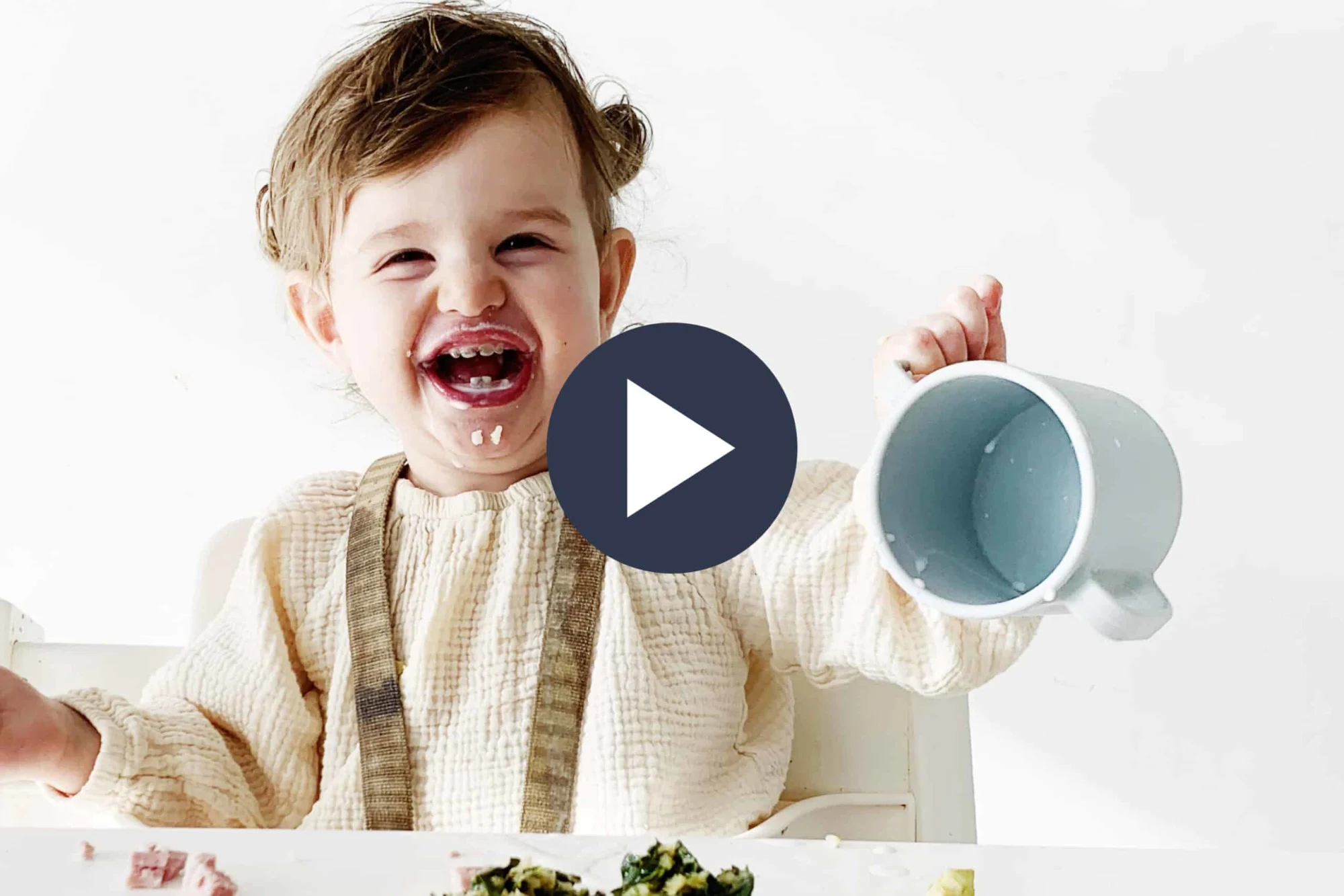 toddler sitting on a high chair laughing and pouring an open cup over the table