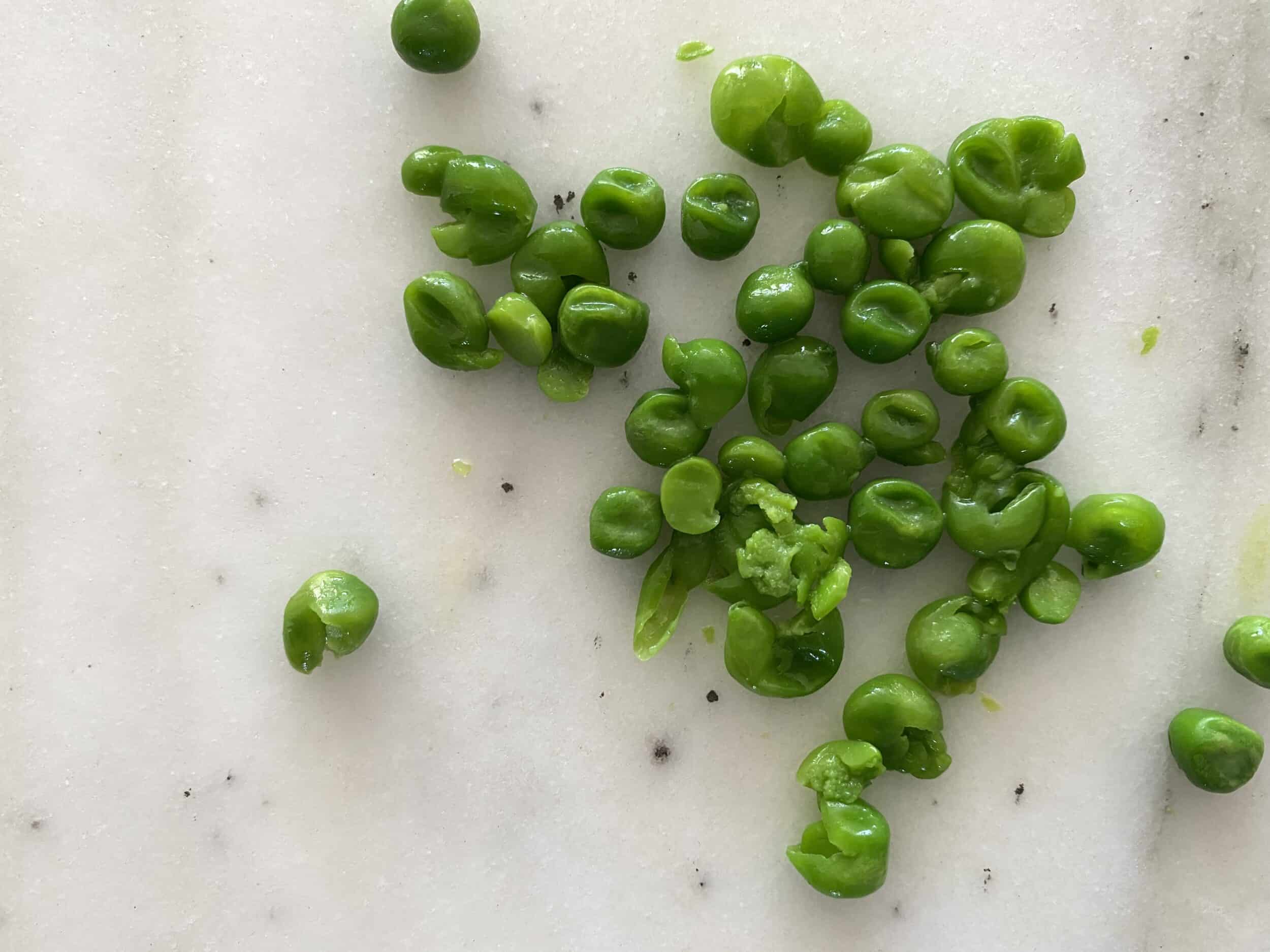 a pile of peas that have been gently flattened with a fork on a white countertop
