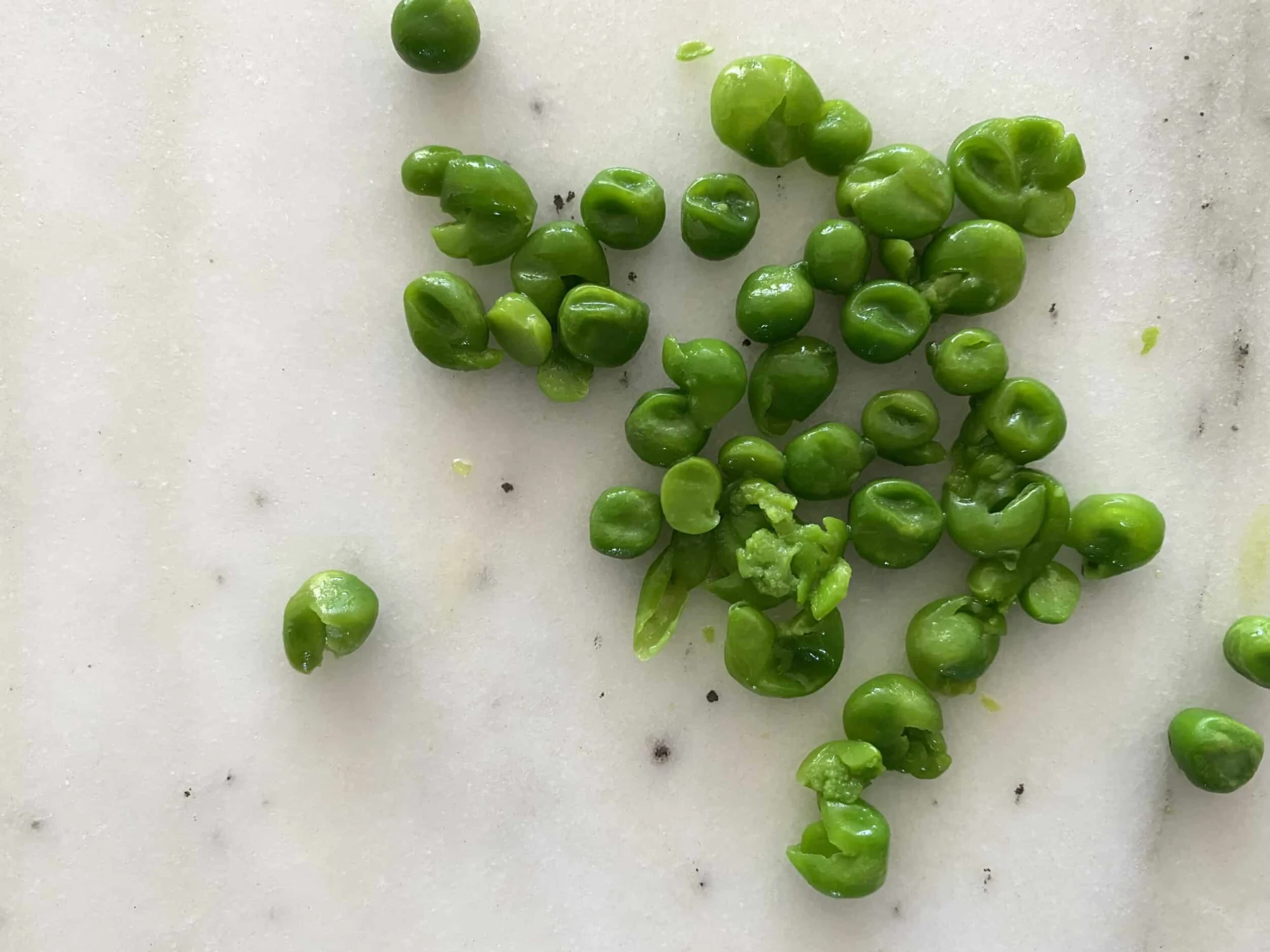 a pile of peas that have been gently flattened with a fork on a white countertop