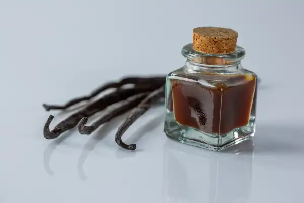 four whole, dried vanilla bean pods next to a small corked glass jar filled with vanilla extract