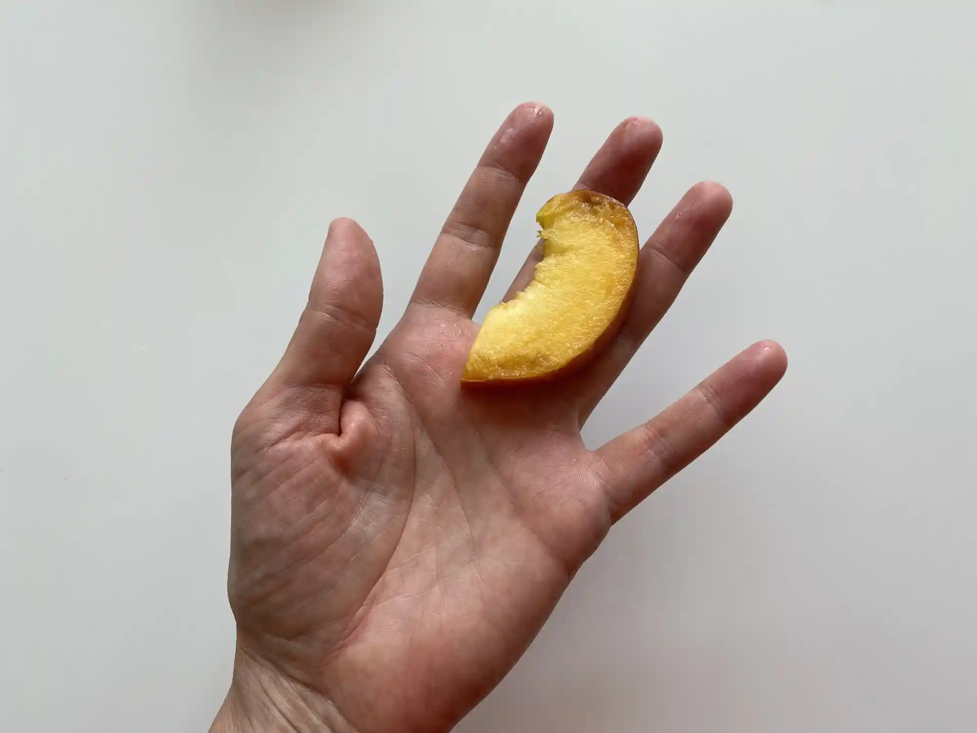 a hand holding a thin slice of peach with the skin still on for babies 9 months +