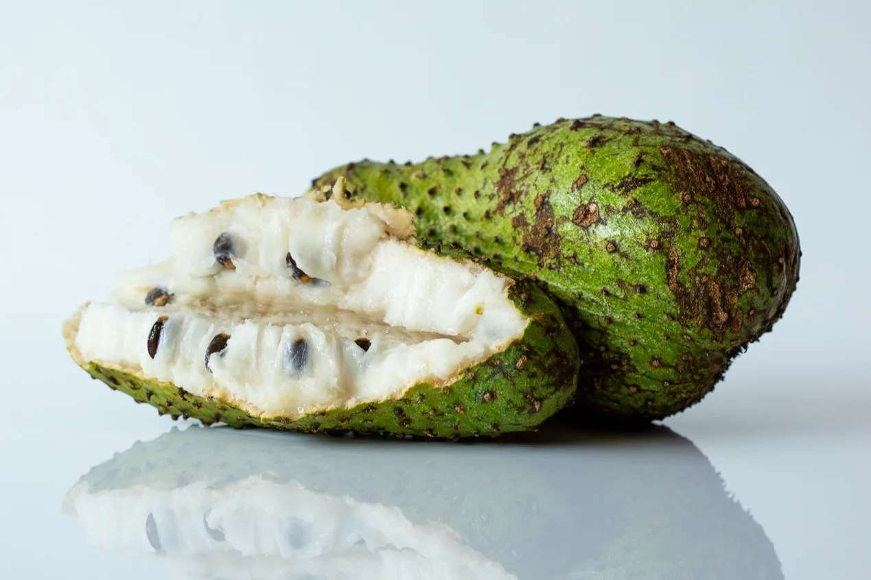a photograph of a whole soursop, with one cut in half showing the inside in front of it