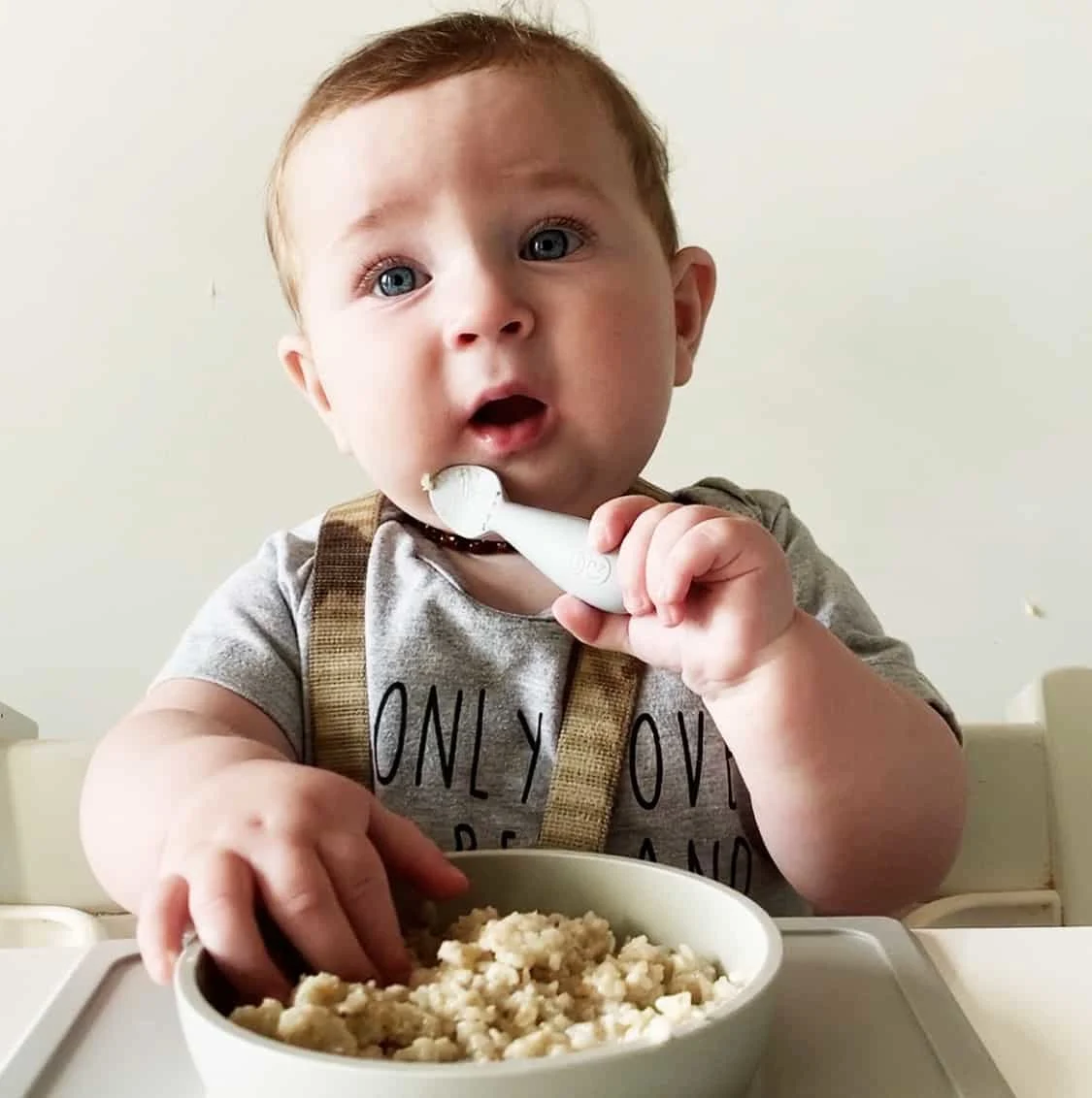 Baby Levi holds a spoon and grabs at some oatmeal