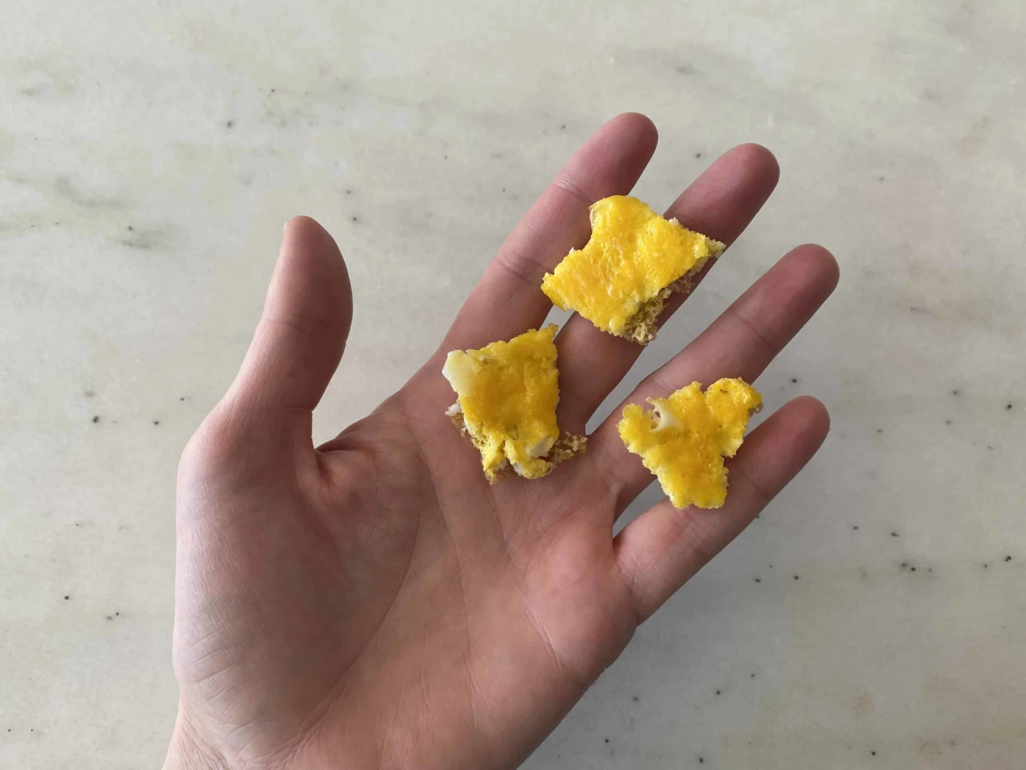 a hand holding three bite-sized pieces of egg omelet for babies 9 months+
