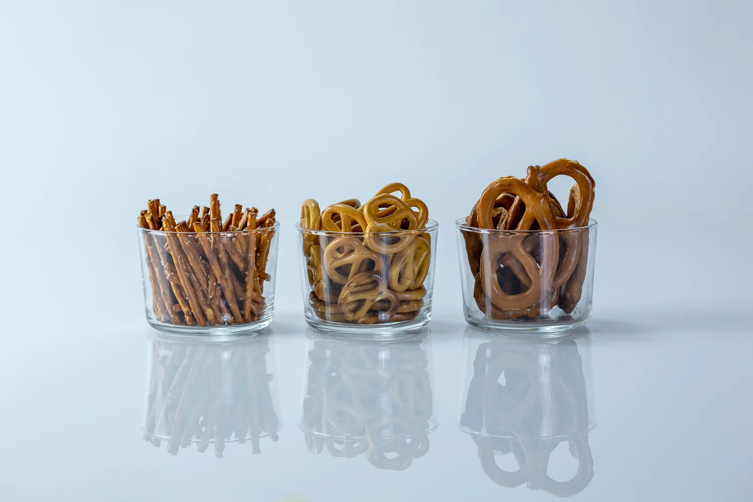 a photograph of three clear cups with different kinds of hard pretzels in them