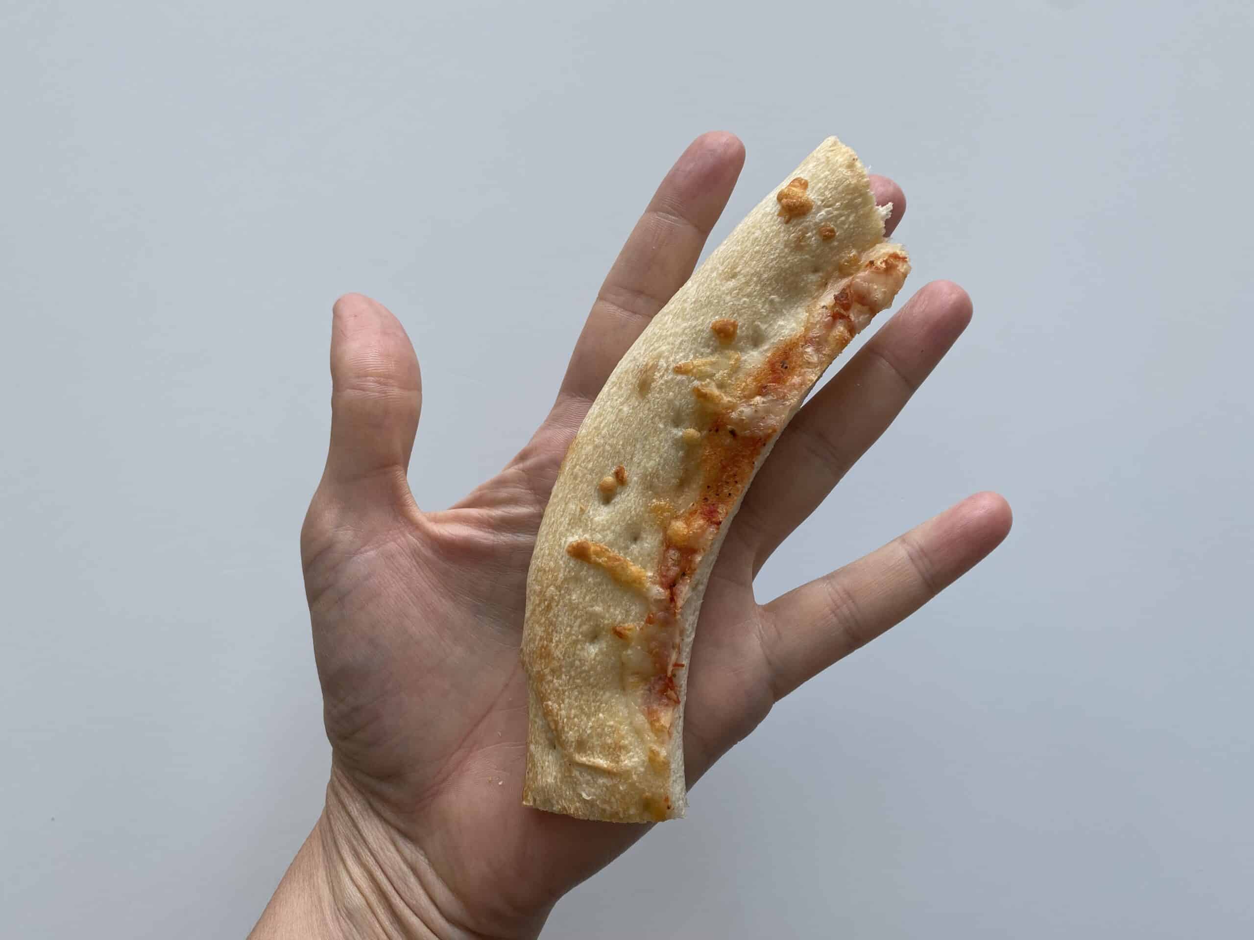 a hand holding a pizza crust with slice cut off for babies 6-8 mos