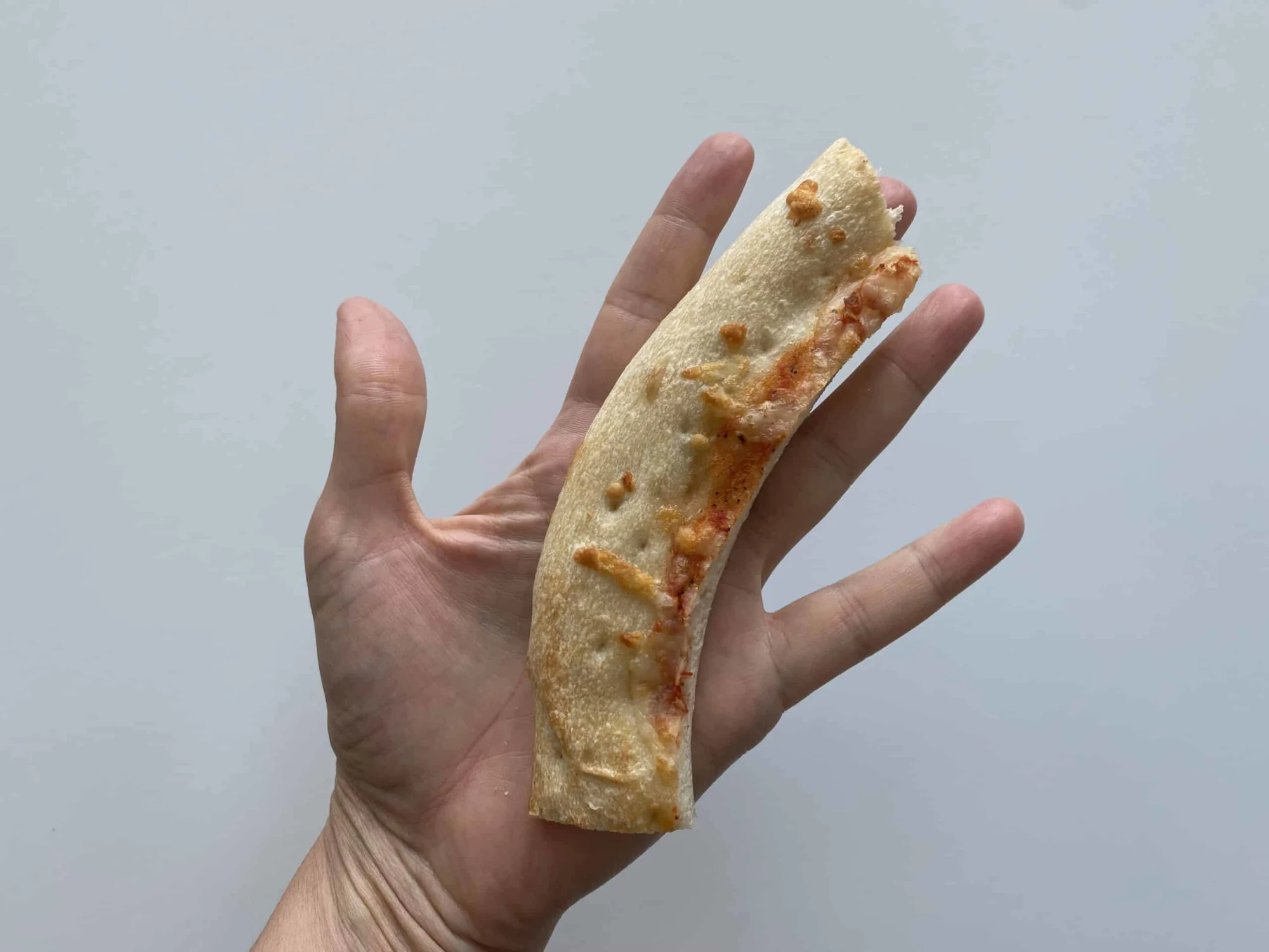 a hand holding a pizza crust with slice cut off for babies 6-8 mos