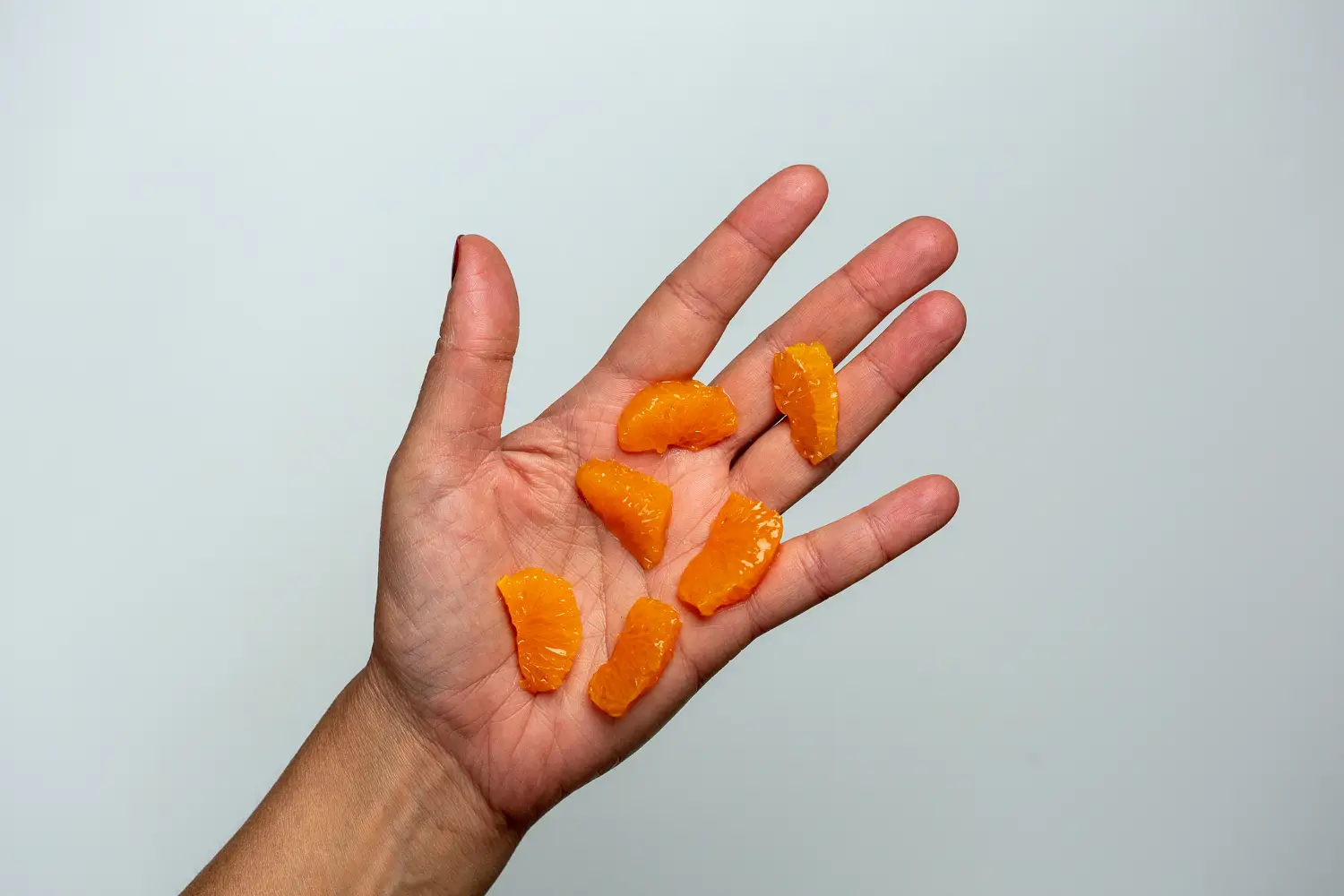 a hand holding six sections of clementine with membranes removed