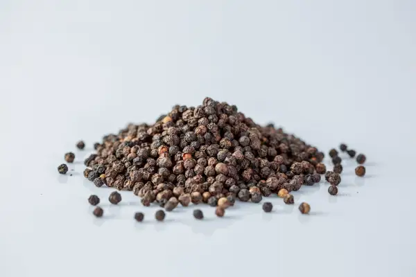 a pile of whole black peppercorns on a white background
