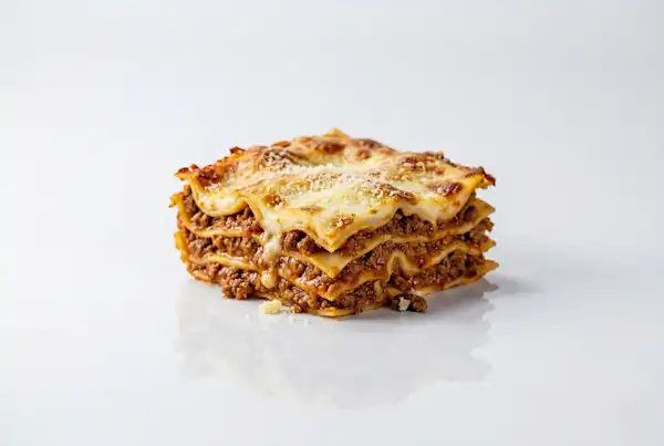 When can babies have lasagna Solid Starts a photograph of a square slice of lasagna on a white background