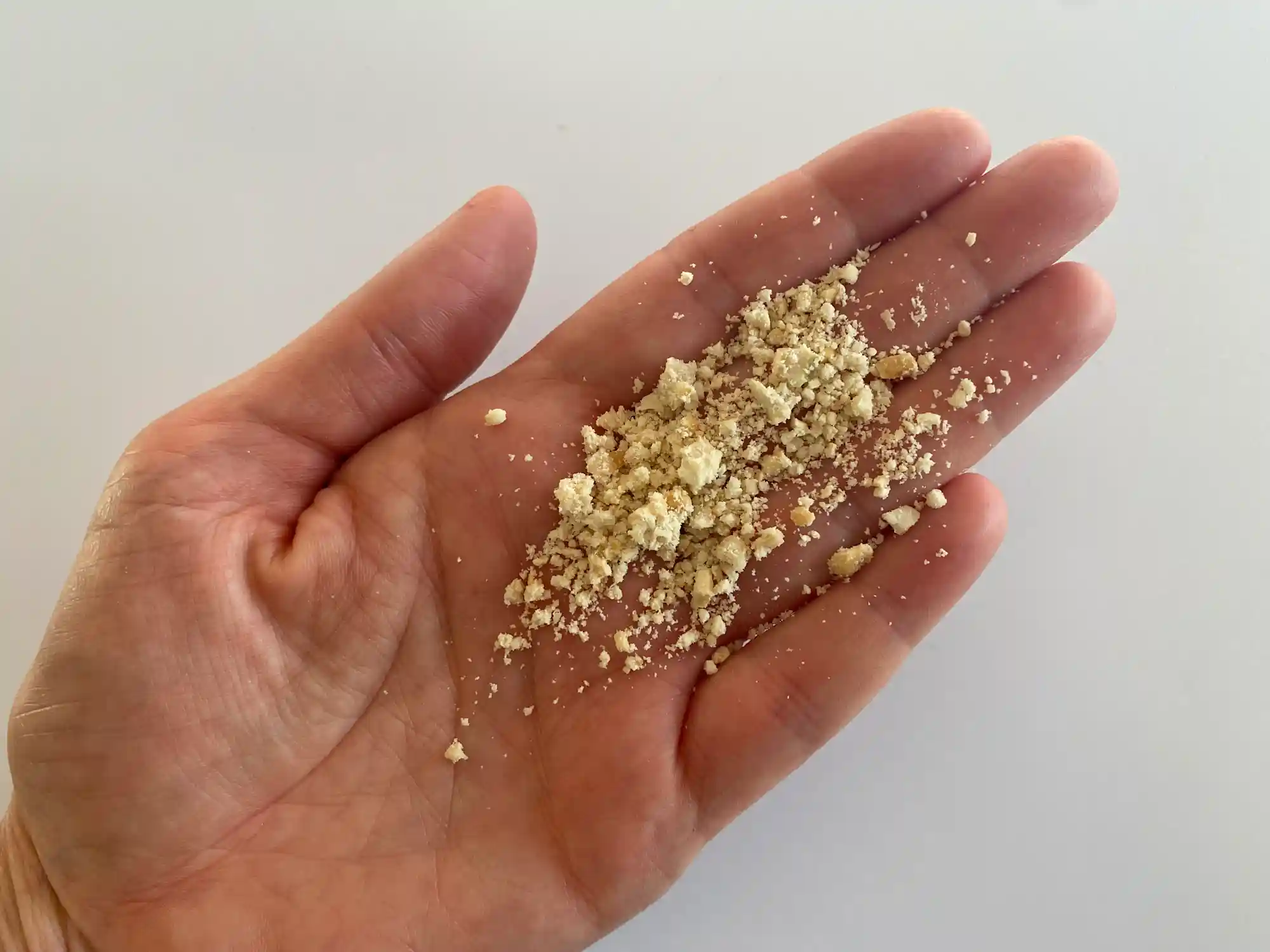 a hand holding a small pile of finely ground cashew pieces