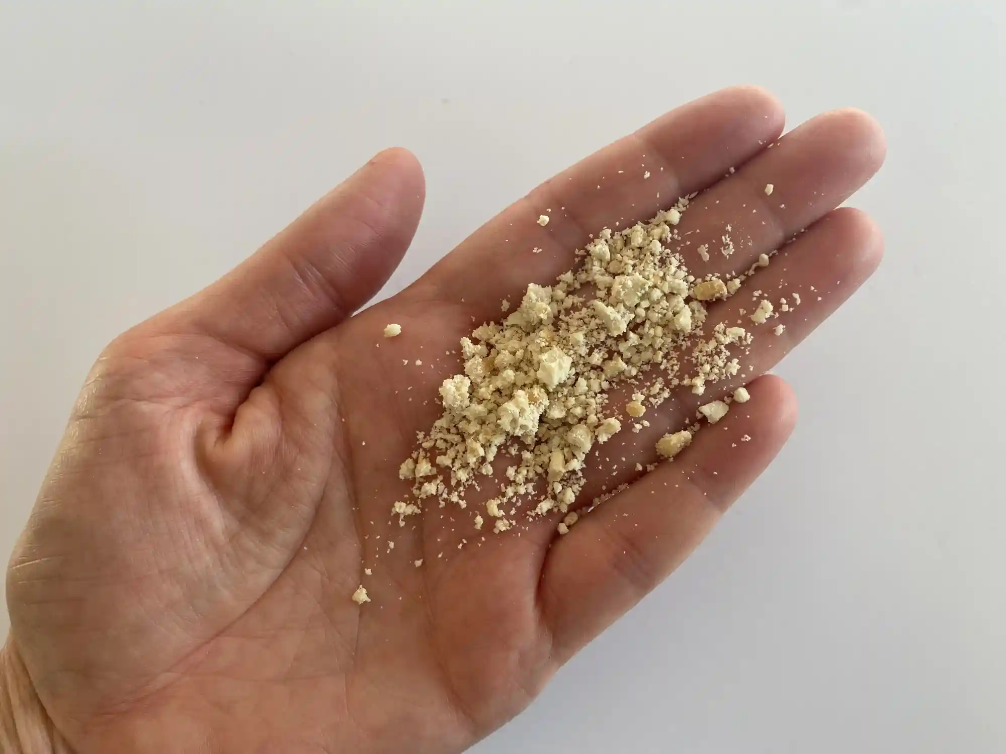 a hand holding a small pile of finely ground cashew pieces