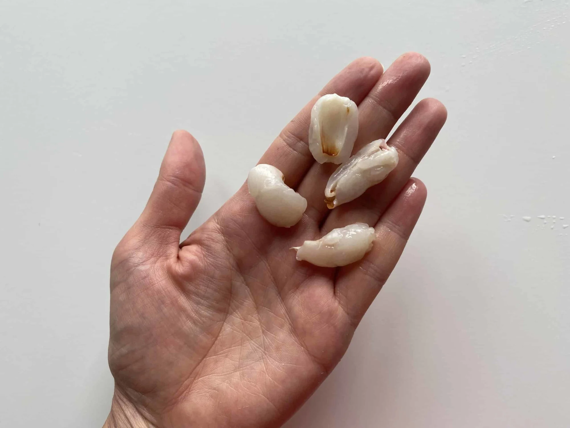 a hand holding four deseeded lychee halves for toddlers 12 months+