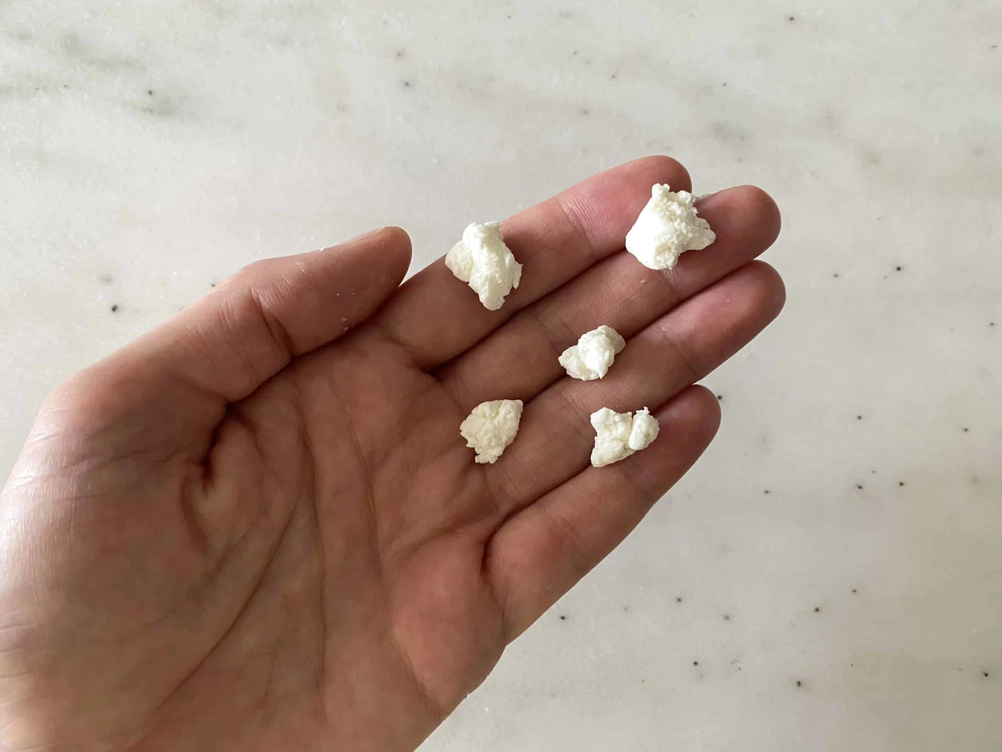 hand holding five pearl size goat cheese crumbles