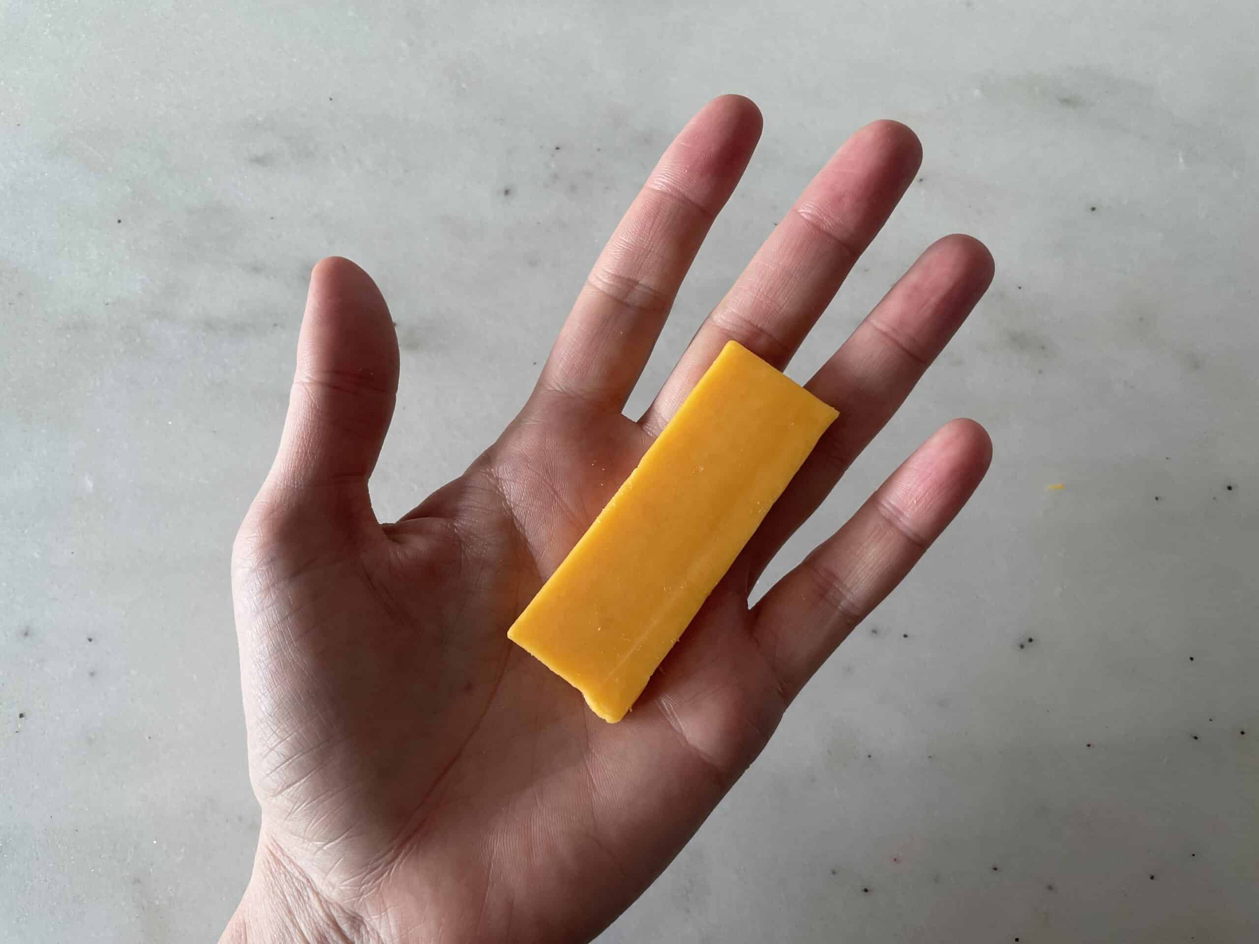 a hand holding a ruler thin slice of cheese for babies 6 months +