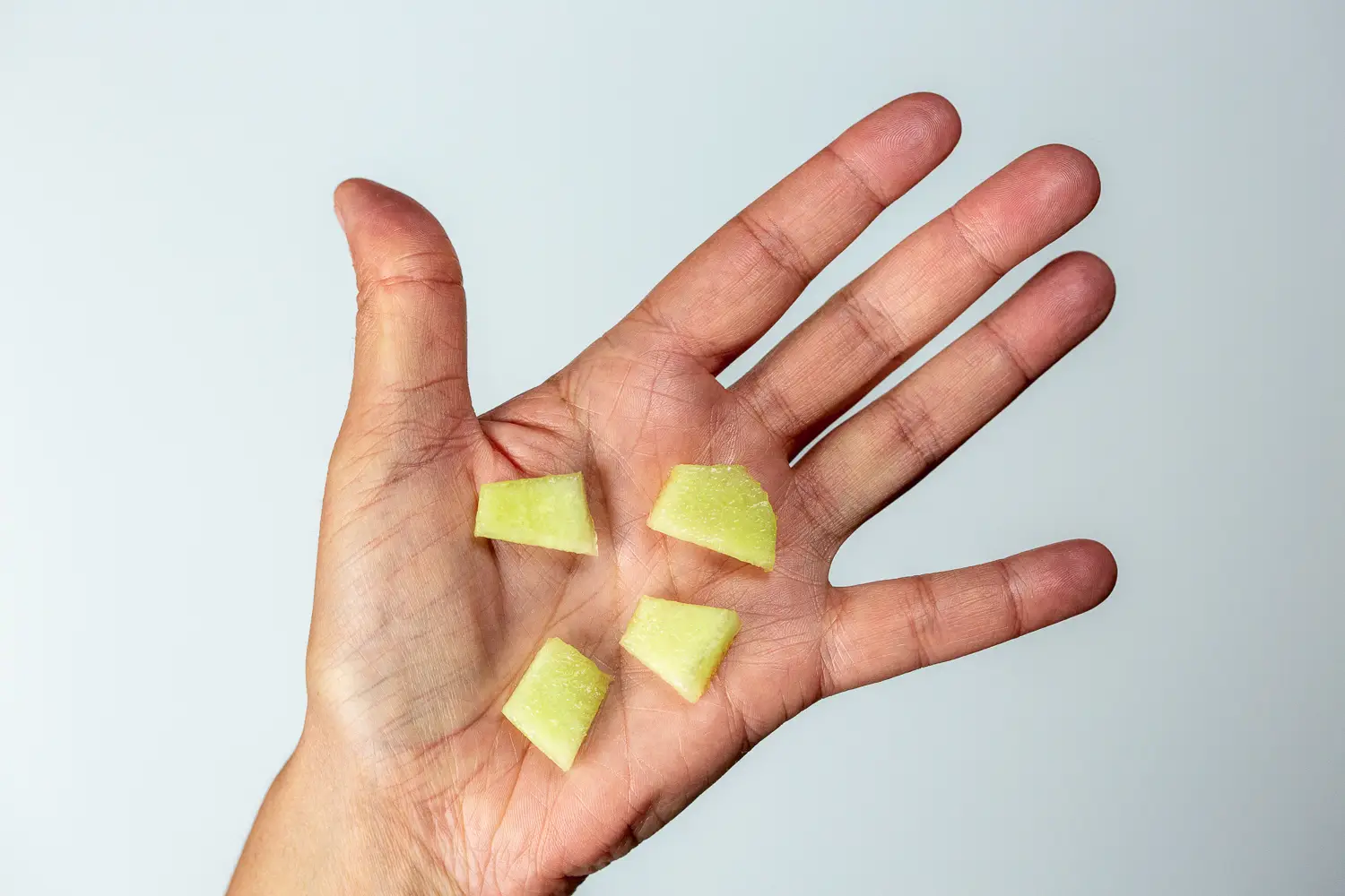 a hand holding four bite-sized pieces cut from a thin slice