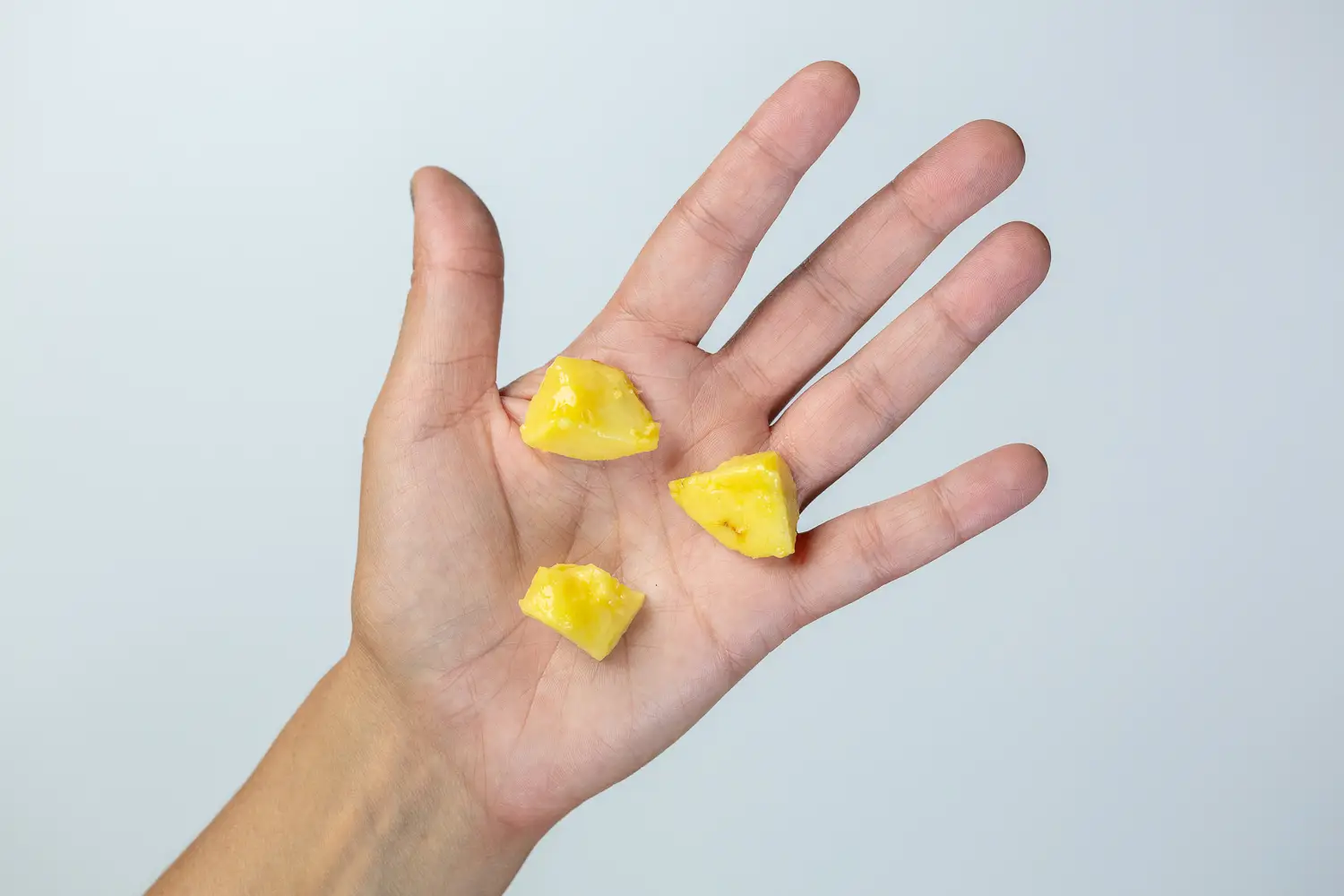 A hand holding three bite-sized pieces of ripe pawpaw