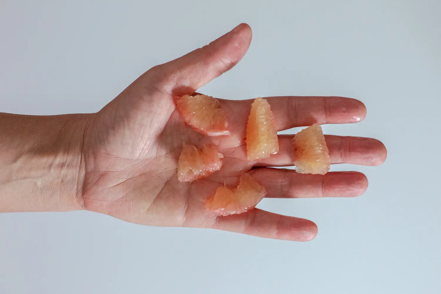 a hand holding five bite-sized pieces of pomelo with peel and membrane removed