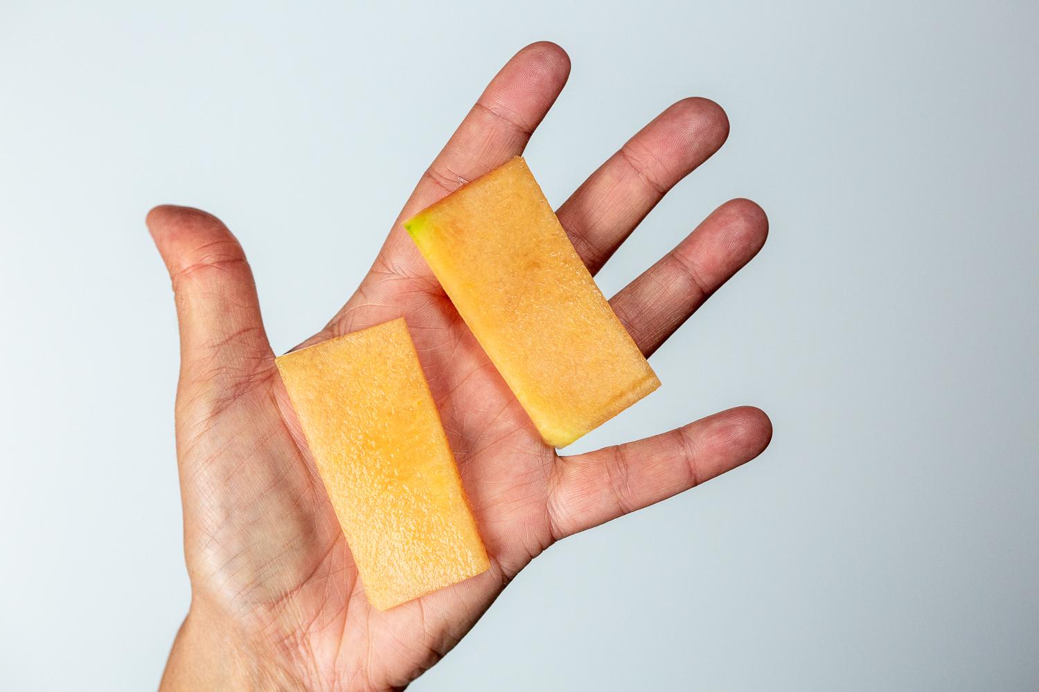 a hand holding two thin rectangular slices of cantaloupe