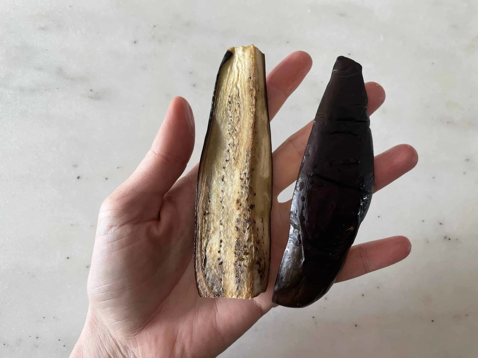 a hand holding two cooked eggplant spears for babies starting solids