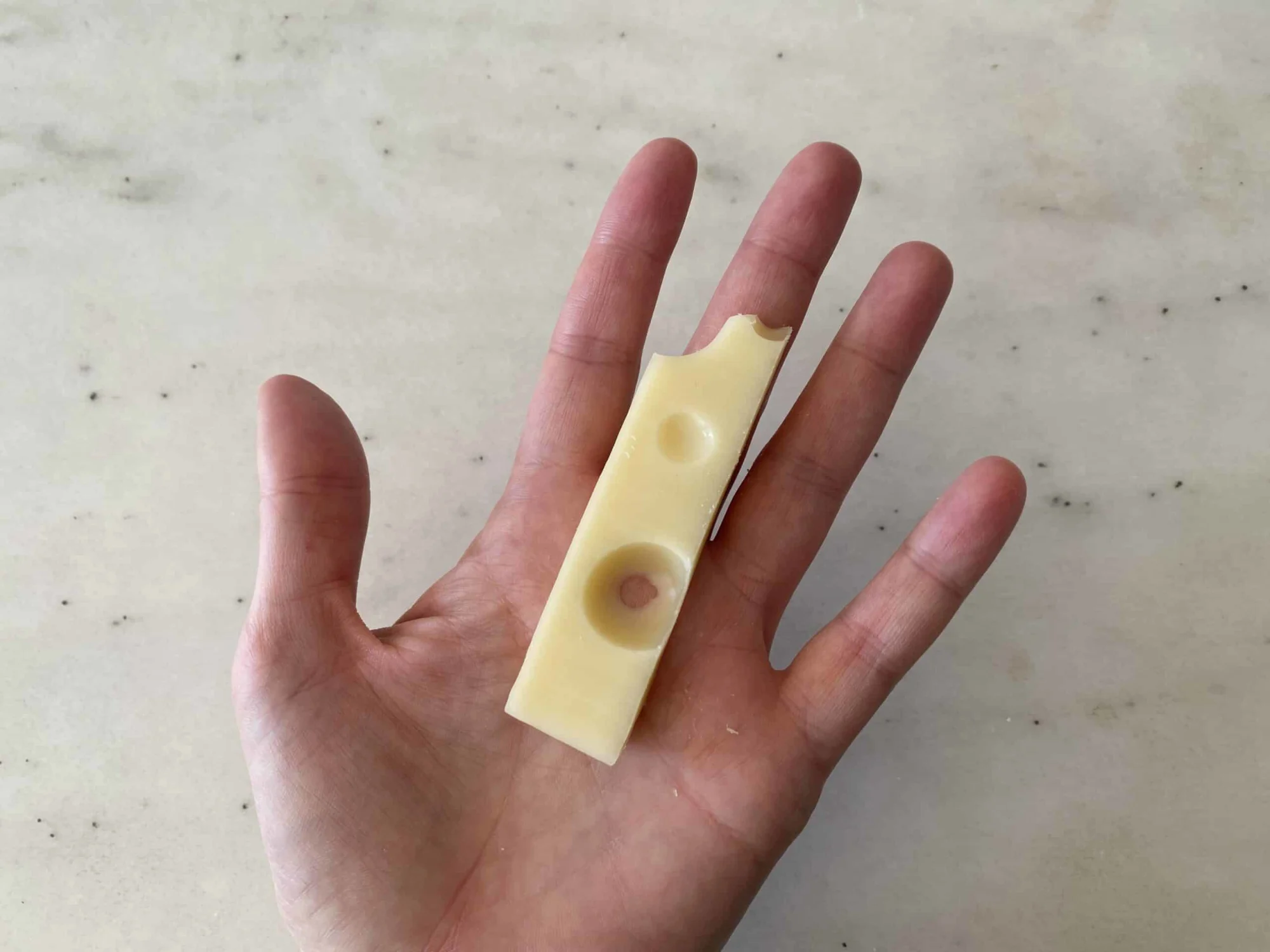 a hand holding a thin slice of swiss cheese for babies 6 months+