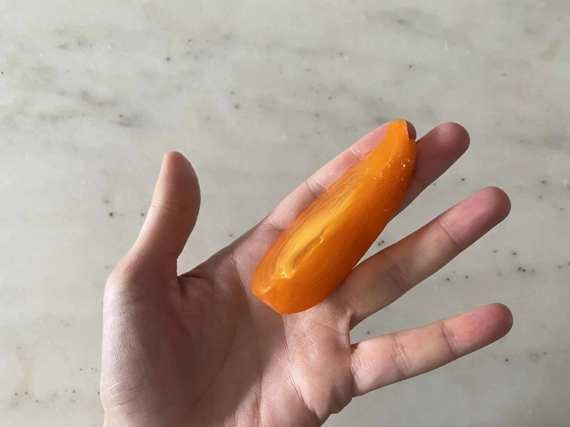 a hand holding one wedge of ripe Hachiya persimmon for babies 6 months +