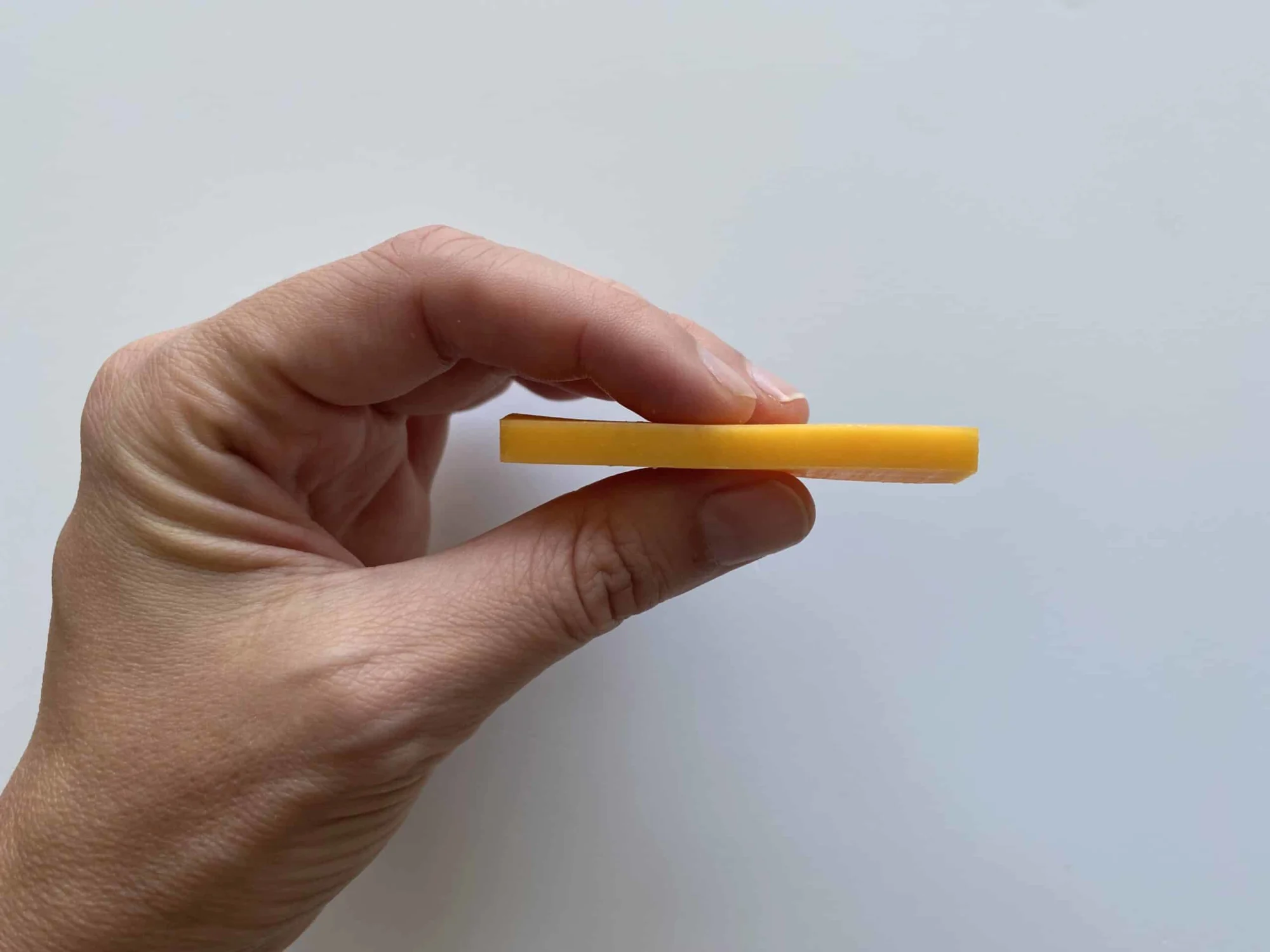 a hand holding a thin slice of colby cheese so you can see its thinness