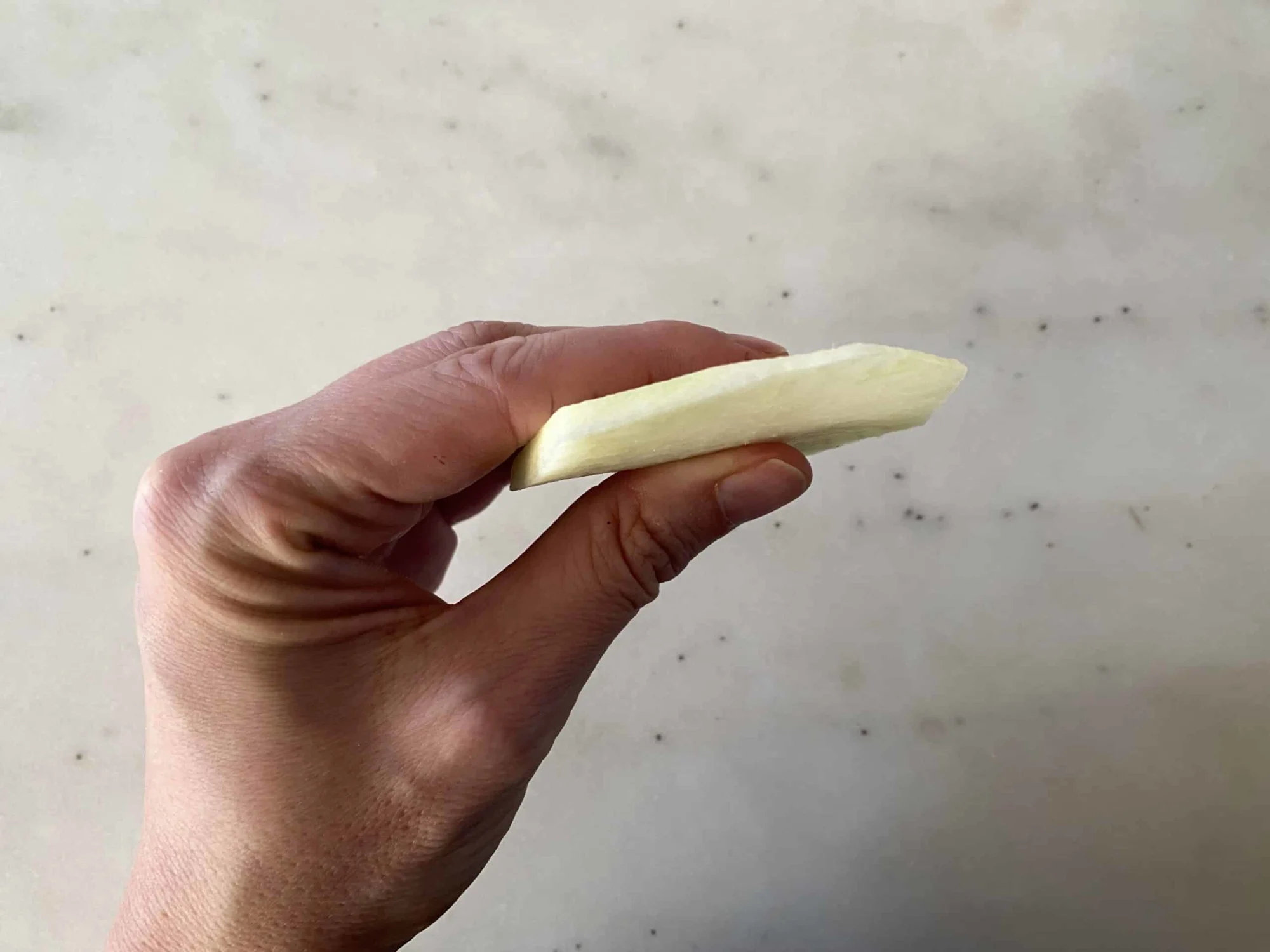 a hand holding a thin cooked wedge of kohlrabi for babies 6 months +