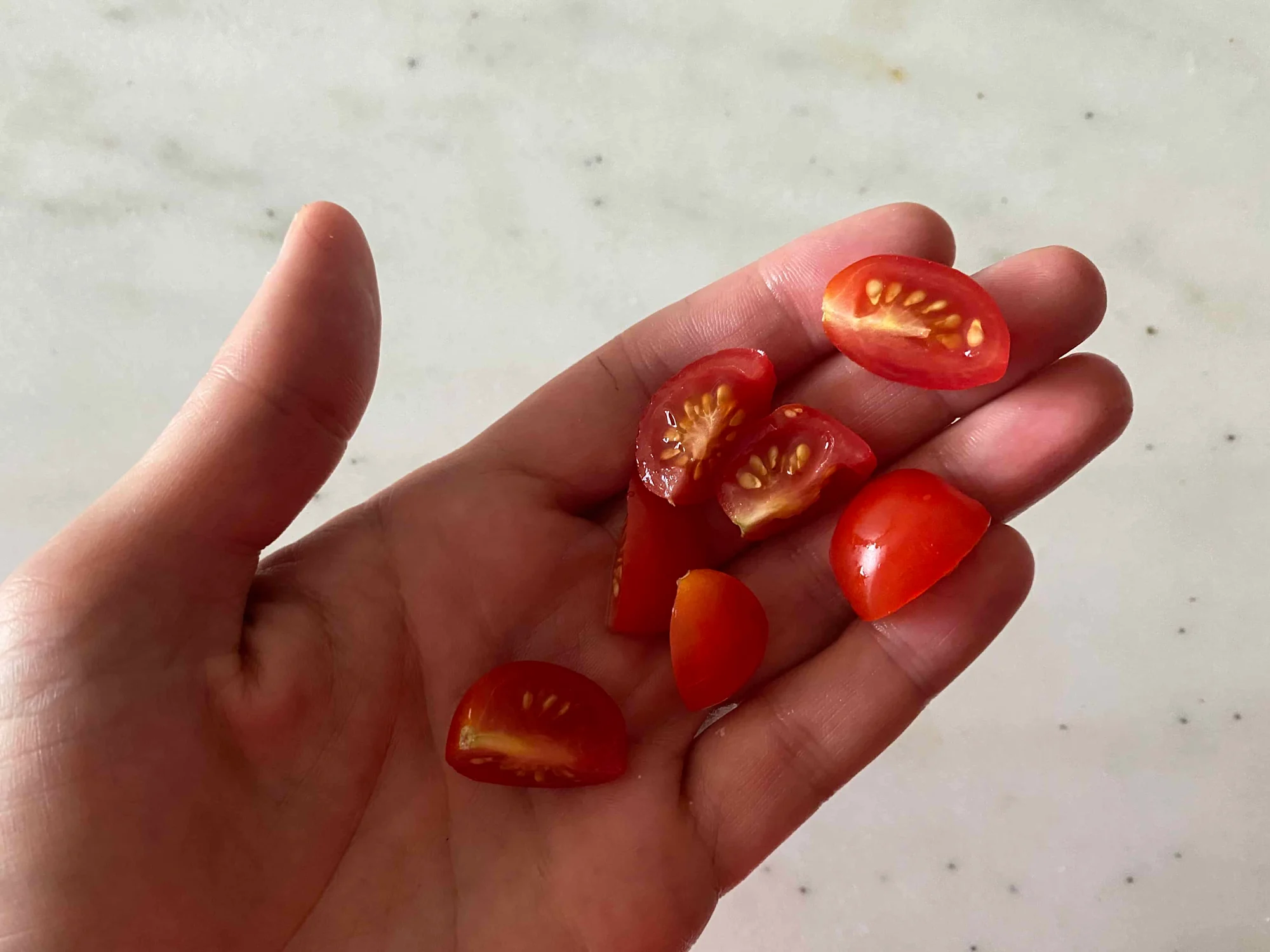 a photograph of a hand holding quartered cherry tomatoes