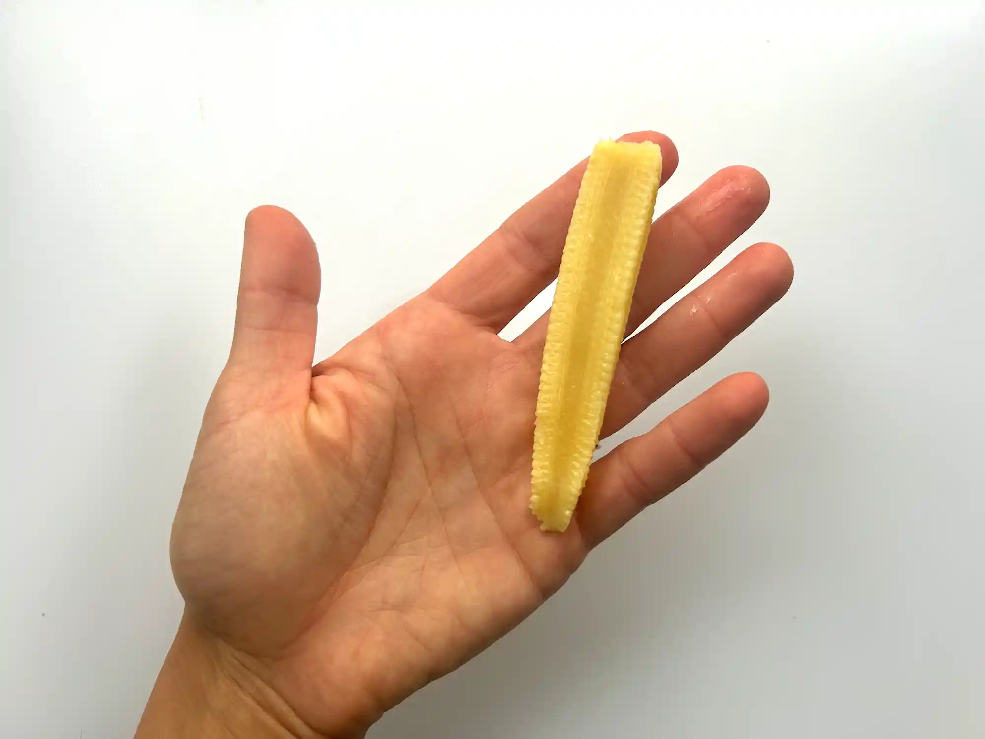 Baby corn cut lengthwise hand pic a photograph of a hand holding a baby corn cut lengthwise