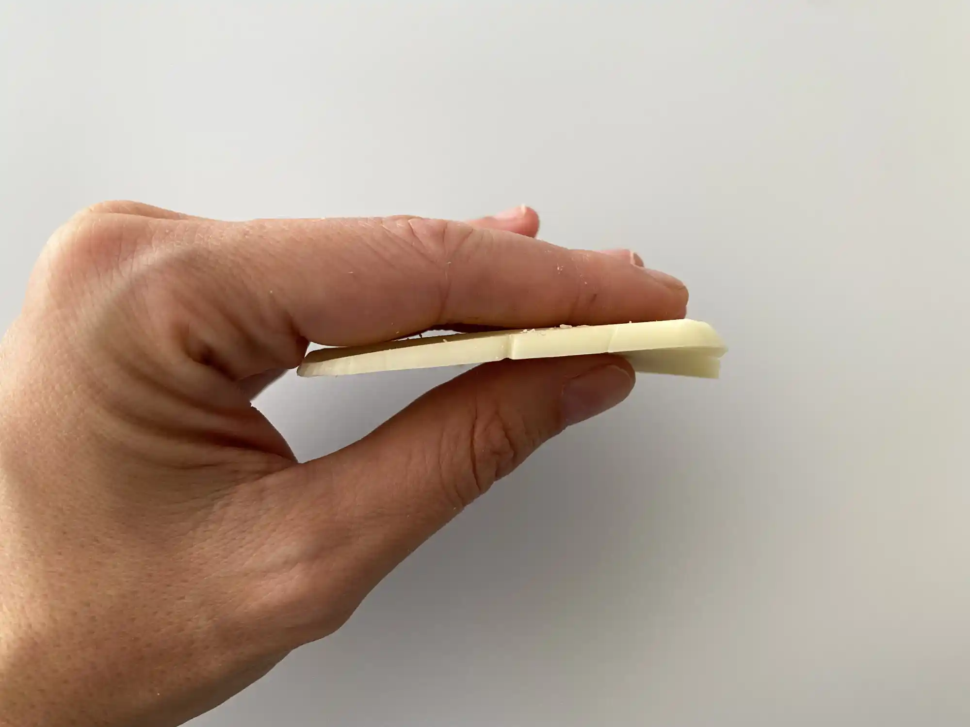 a hand holding a thin slice of quesillo sideways to demonstrate its thickness