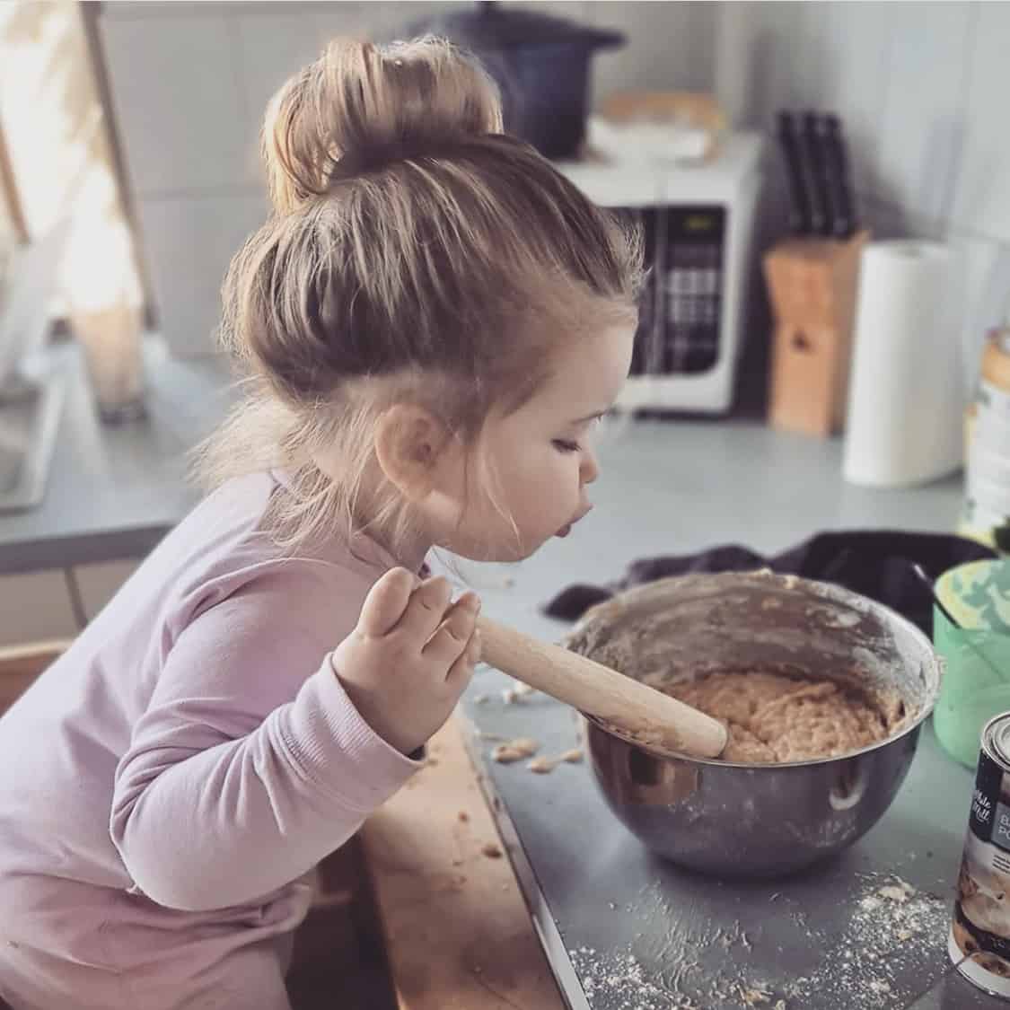 A toddler girl mixing a bowl of cake batter with a wooden spoon.