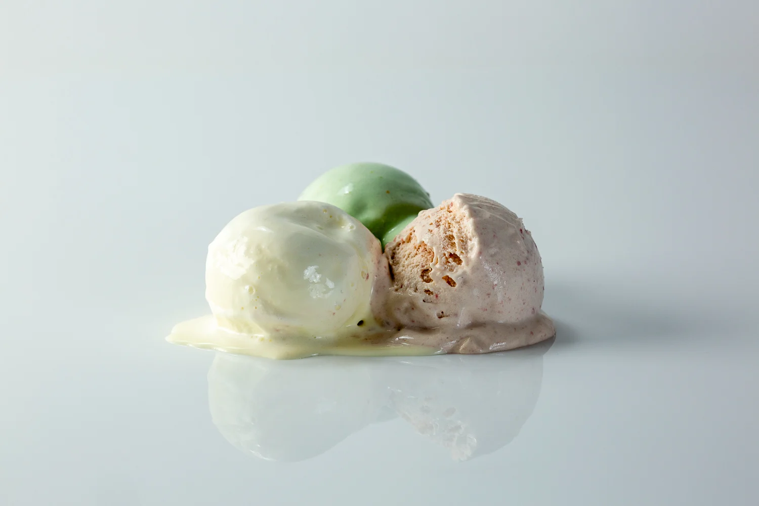 three scoops of ice cream on a white background, one white, one green, and one pink