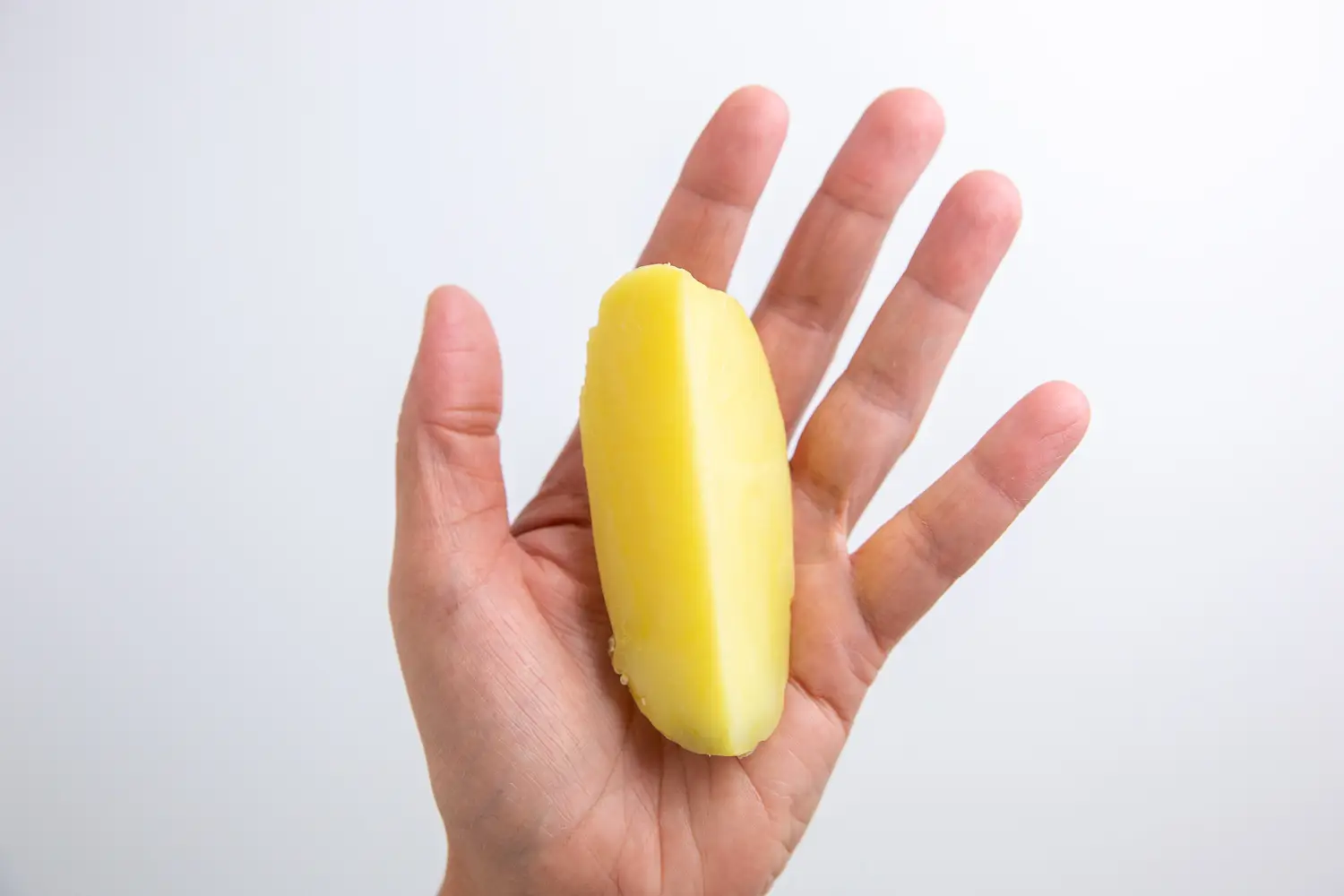 a photograph of a hand holding one long cooked wedge of potato for babies 6 months+