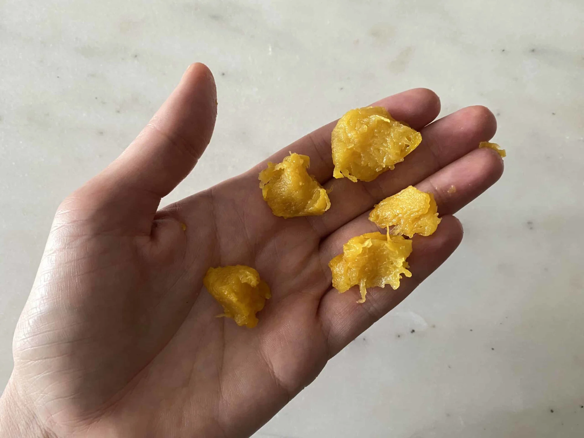 a hand holding small pieces of cooked, orange squash for babies starting solids