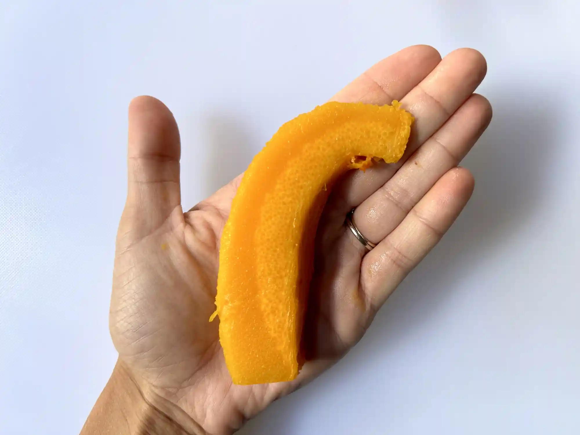 a photograph of a hand holding a large wedge of cooked pumpkin