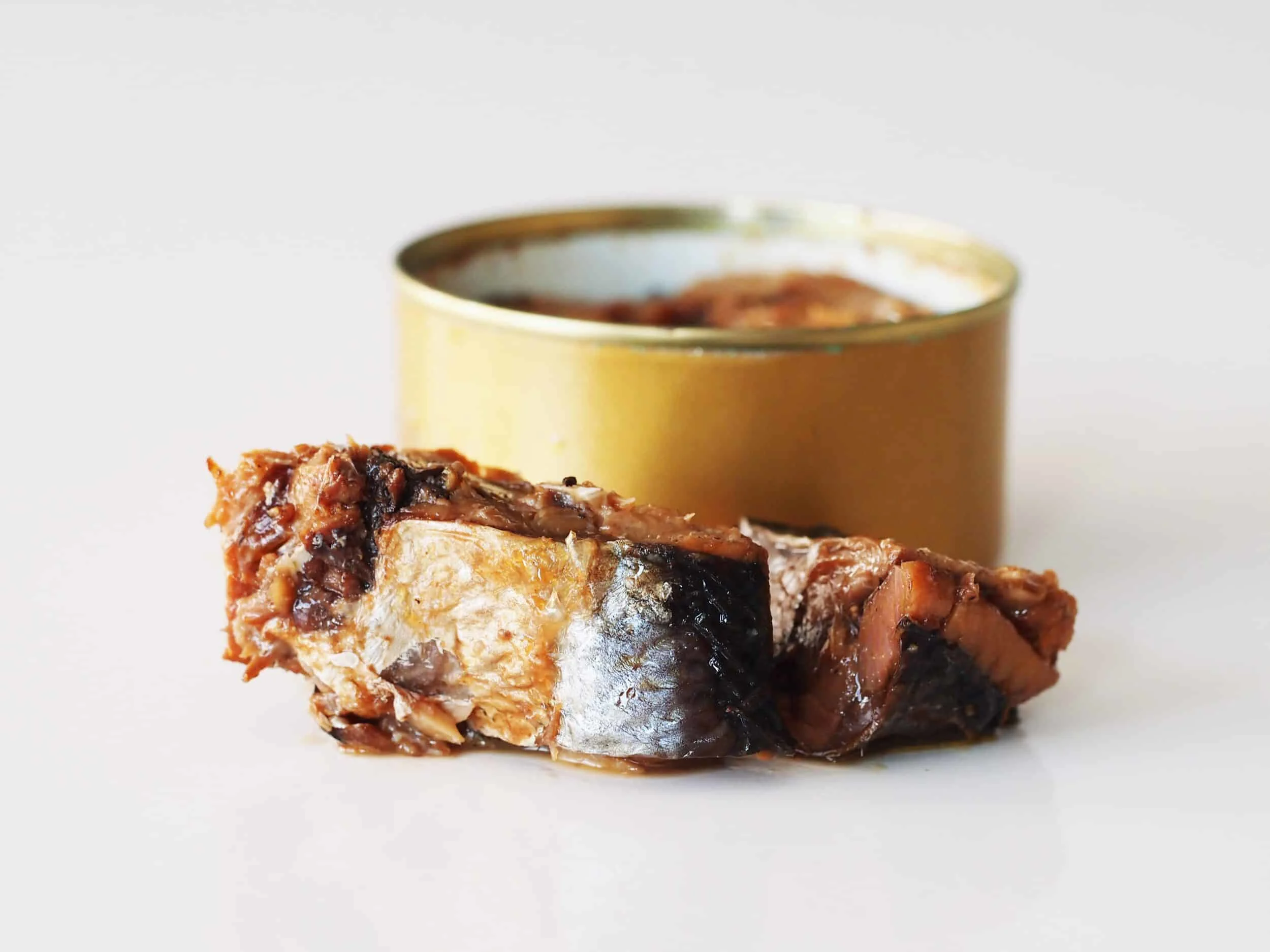 A gold can of herring with no label and a herring filet in front of it before being prepared for babies starting solids