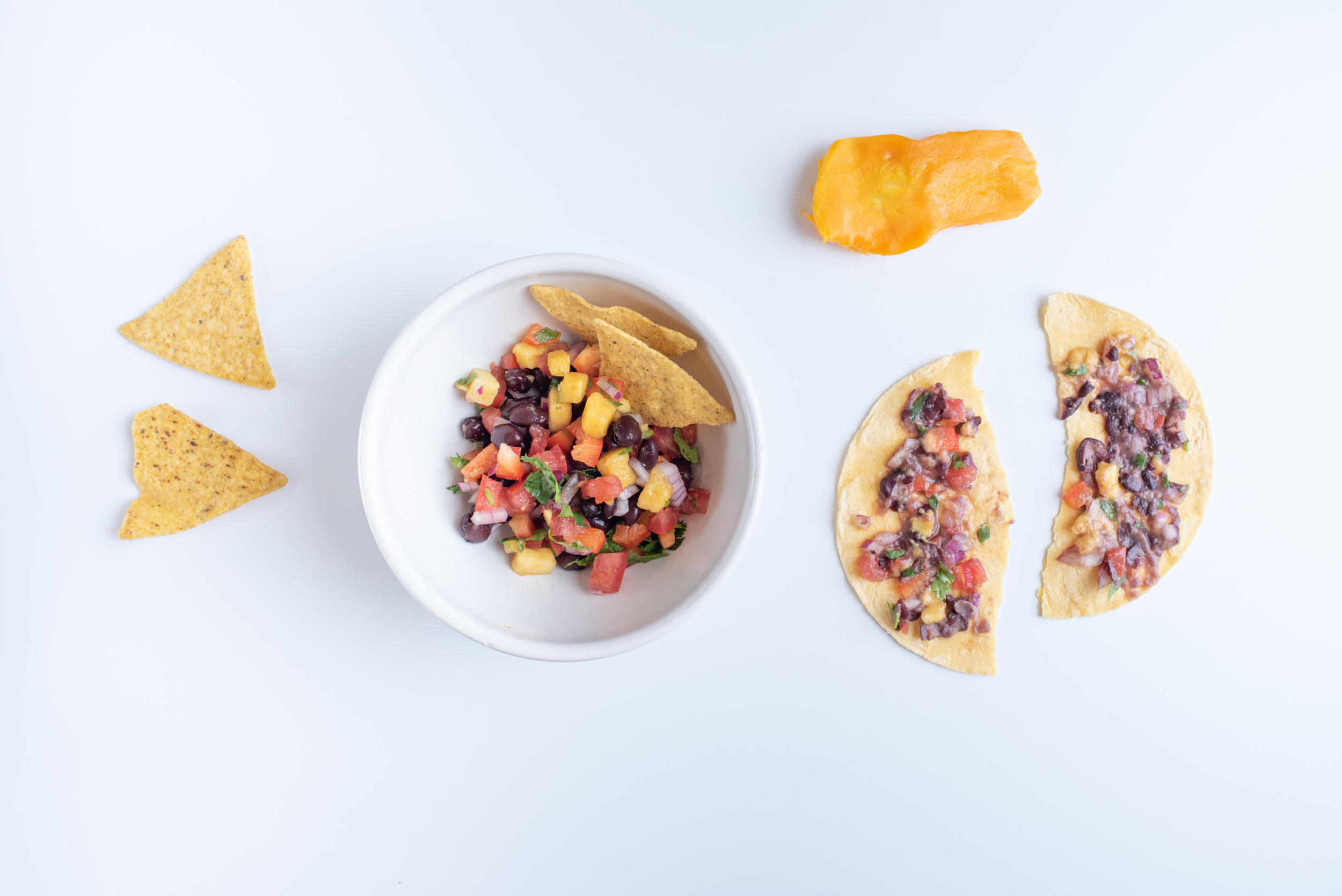 a round bowl with salsa and tortilla chips for an adult next to two soft corn tortilla halves spread with the same salsa, with a cooked sweet potato half above the tortilla