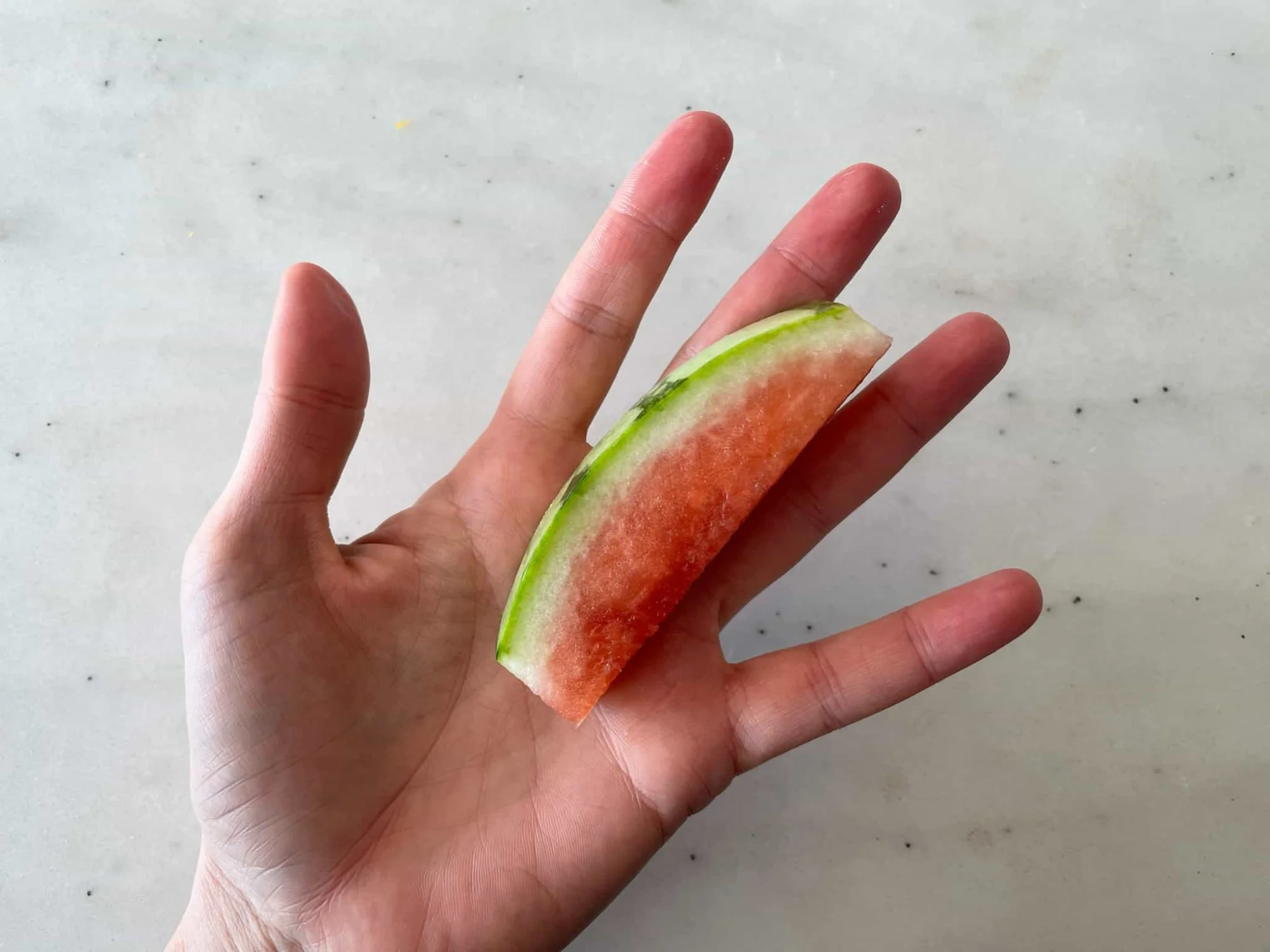 a hand holding a thick slice of watermelon rind with most of the flesh cut off for babies 6 months+