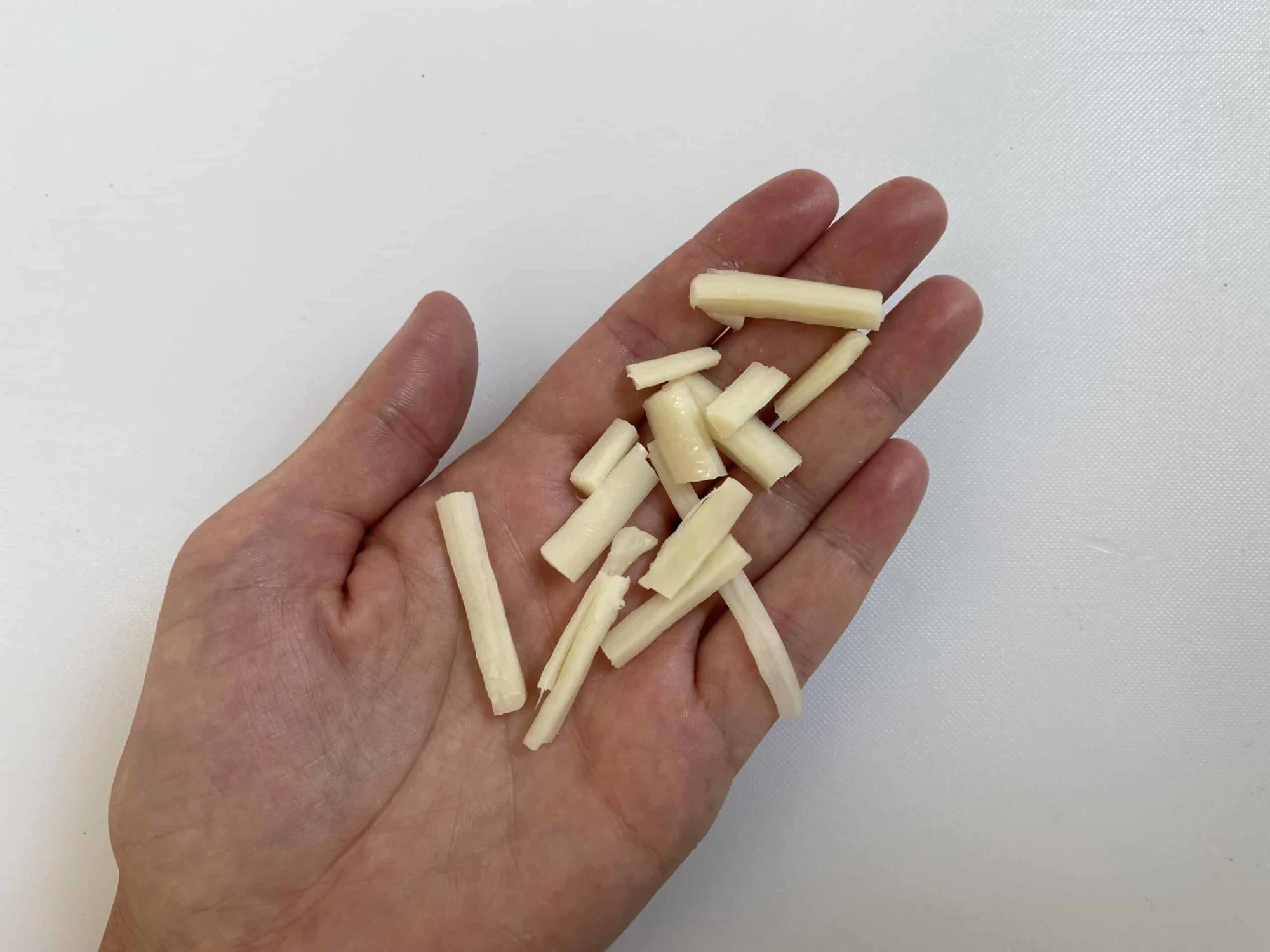 a hand holding a small pile of string cheese pieces (made by pulling the cheese into thin strands and then pulling the strands into small pieces)