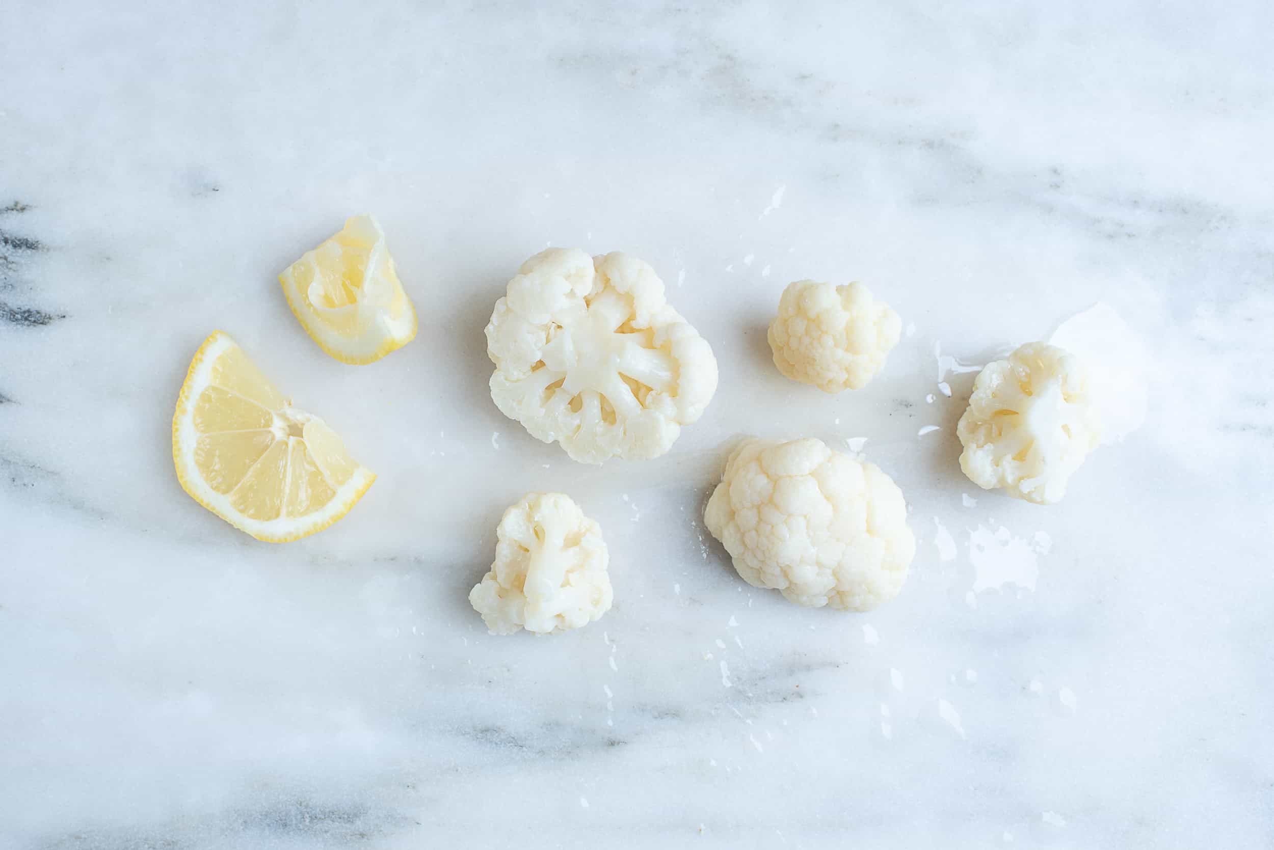 five steamed cauliflower florets sitting on a countertop with 2 slices of lemon next to them