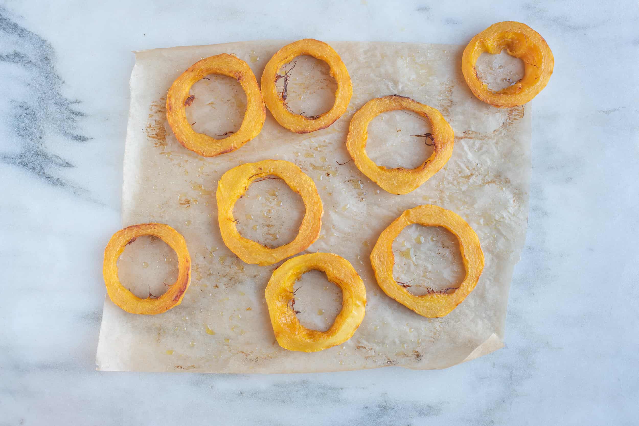 eight roasted delicata squash rings on a piece of parchment paper on a white background for babies starting solids